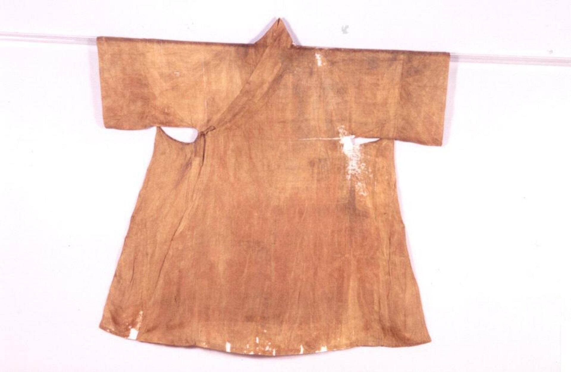 An ancient garment laid out on a white background. It is sepia-toned and slightly torn, reflecting its age.