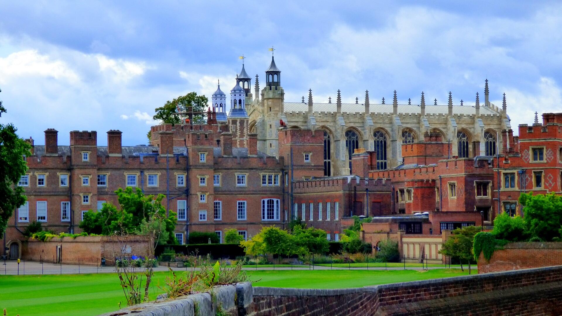 A brick building with a larger sandstone chapel behind it, surrounded by a vibrant green lawn.