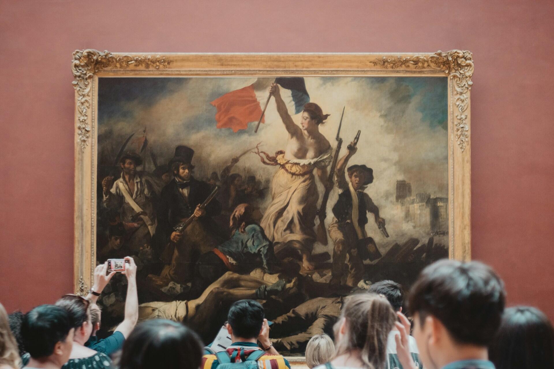 Museum visitors photograph Eugène Delacroix’s framed painting of Liberty leading armed revolutionaries over fallen figures.