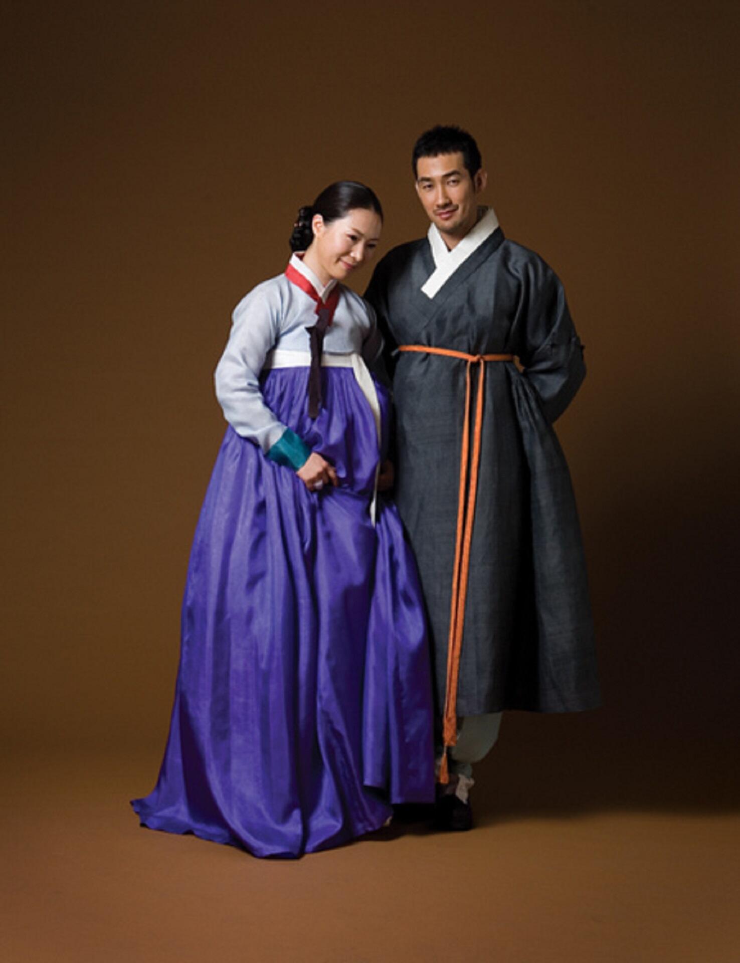 A man and a woman wearing traditional Korean hanbok that is colourful but not decorated. They appear cosy and comfortable.