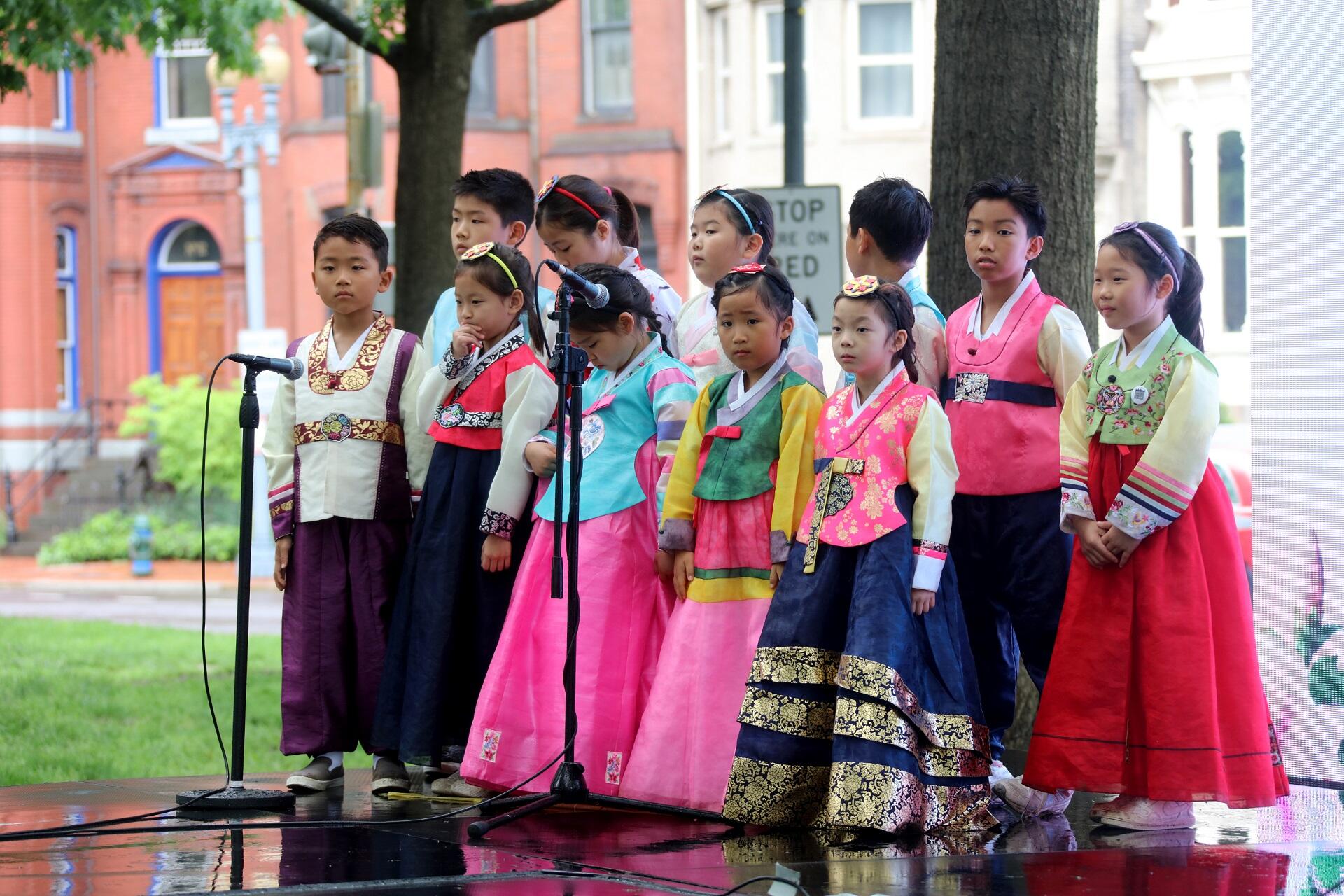 A group of children wearing various styles of Korean hanbok while standing outdoors. The mood is solemn and excited.