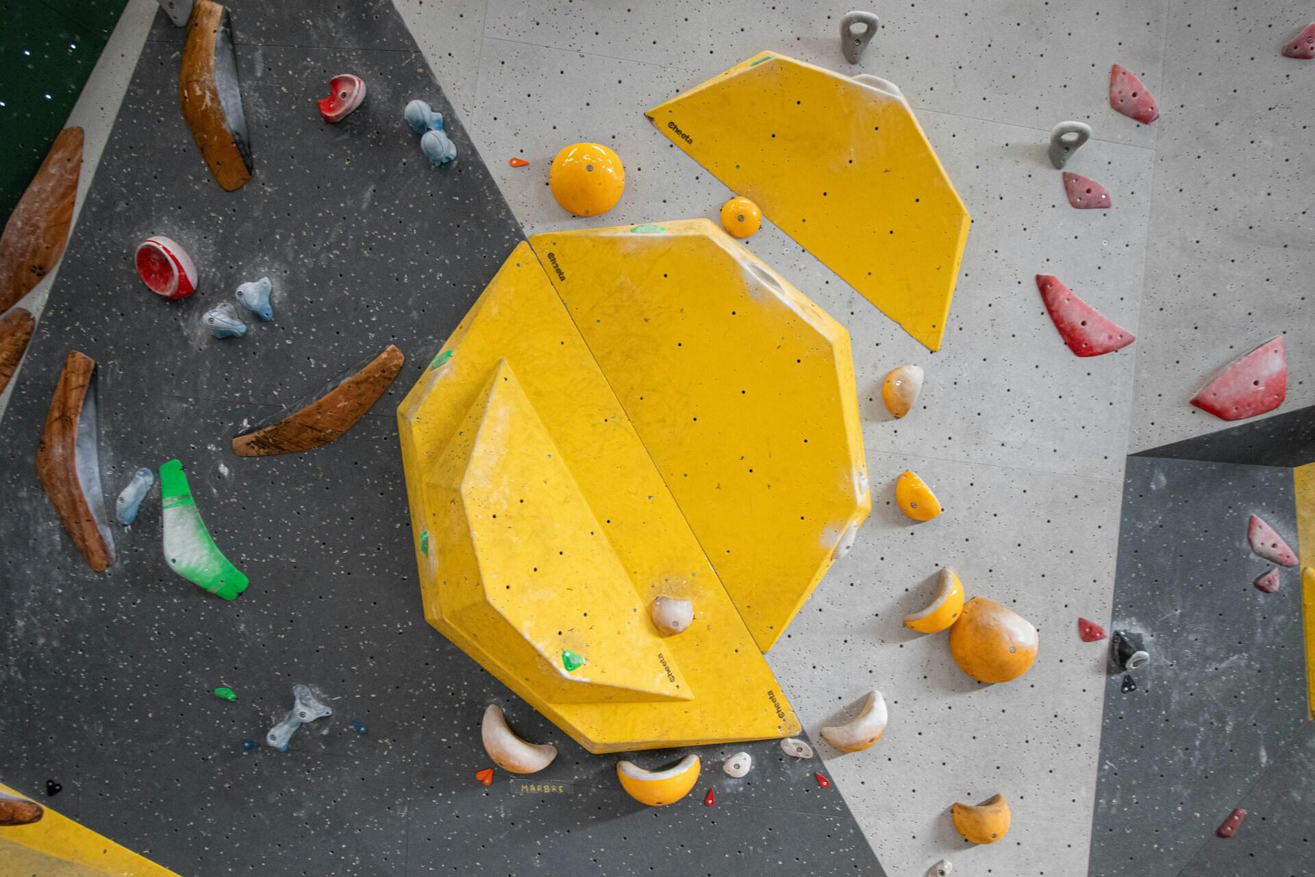 Indoor bouldering wall with large yellow volumes and coloured climbing holds
