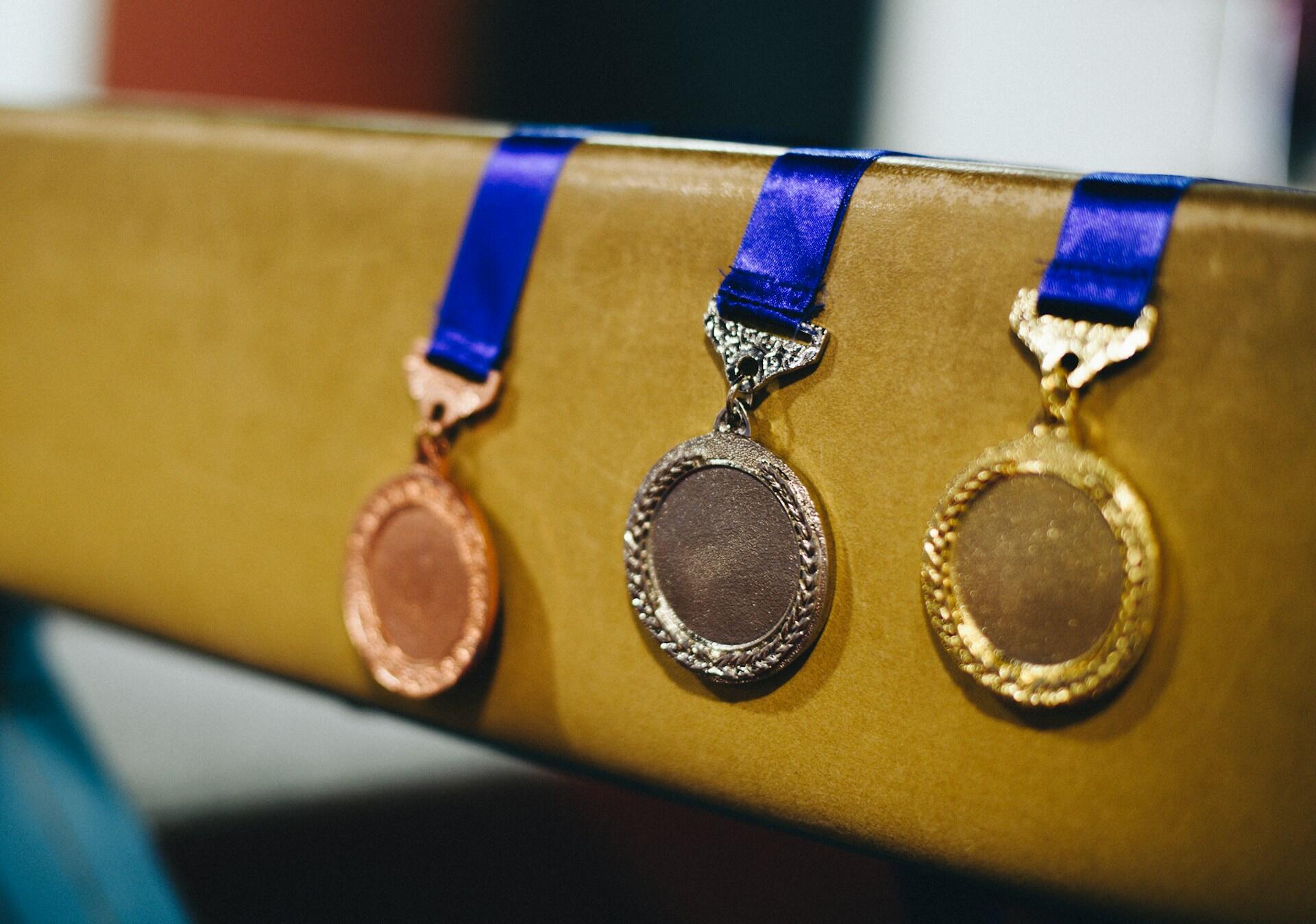 Gold, silver, and bronze medals with blue ribbons draped over a draped over a golden block.