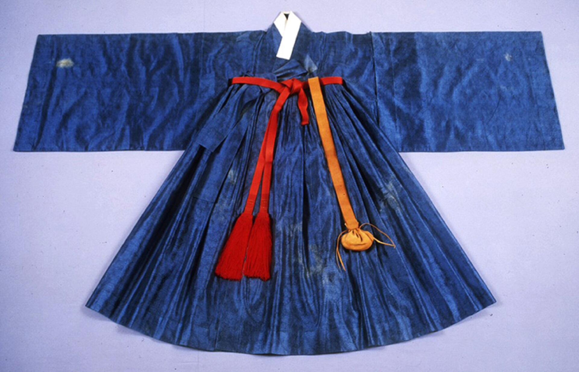 A traditional Korean garment featuring a flared skirt and a wide-sleeved jacket, adorned with red and gold belts.