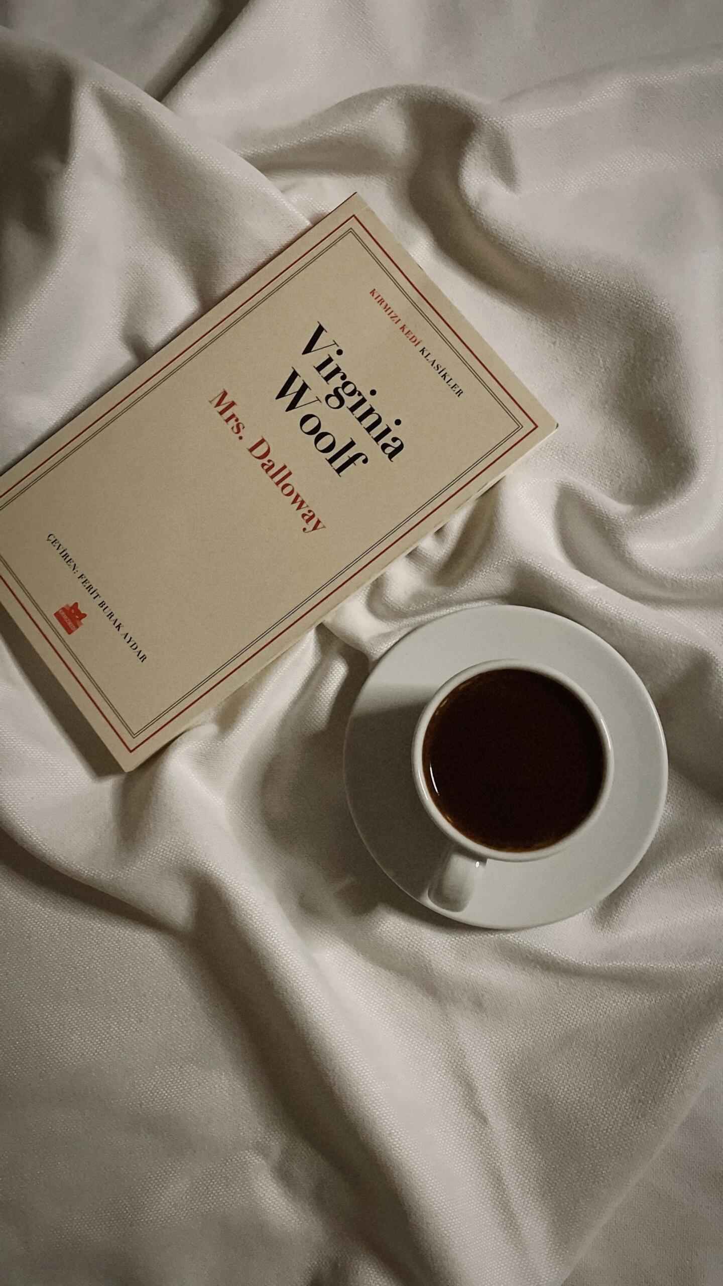 Virginia Woolf’s book Mrs Dalloway lies on white satin beside a white cup and saucer filled with dark coffee.