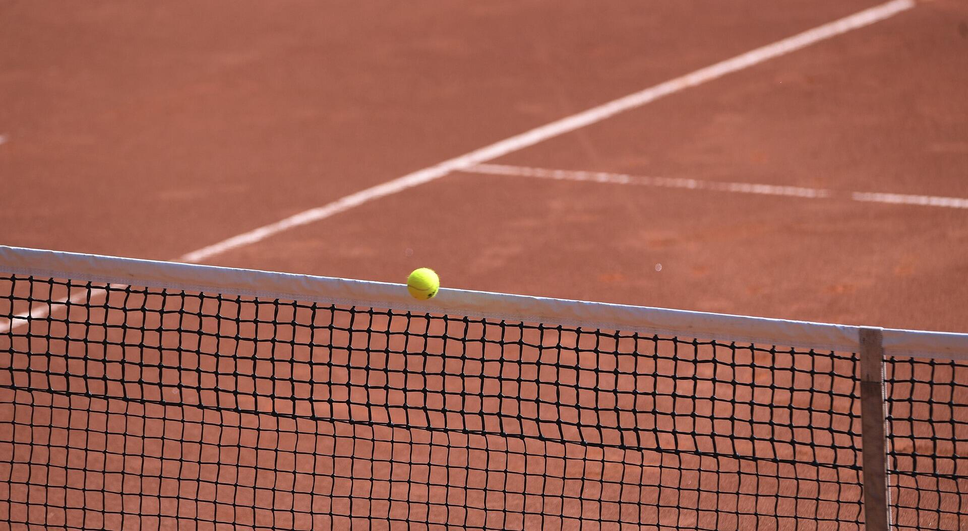 Close up of a clay court, tennis ball impacting the net