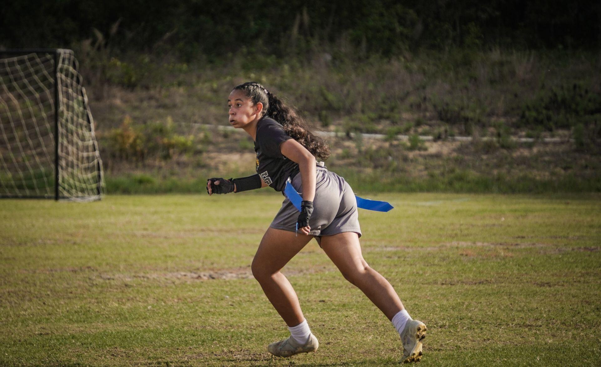 Female flag football athlete sprinting on a court.