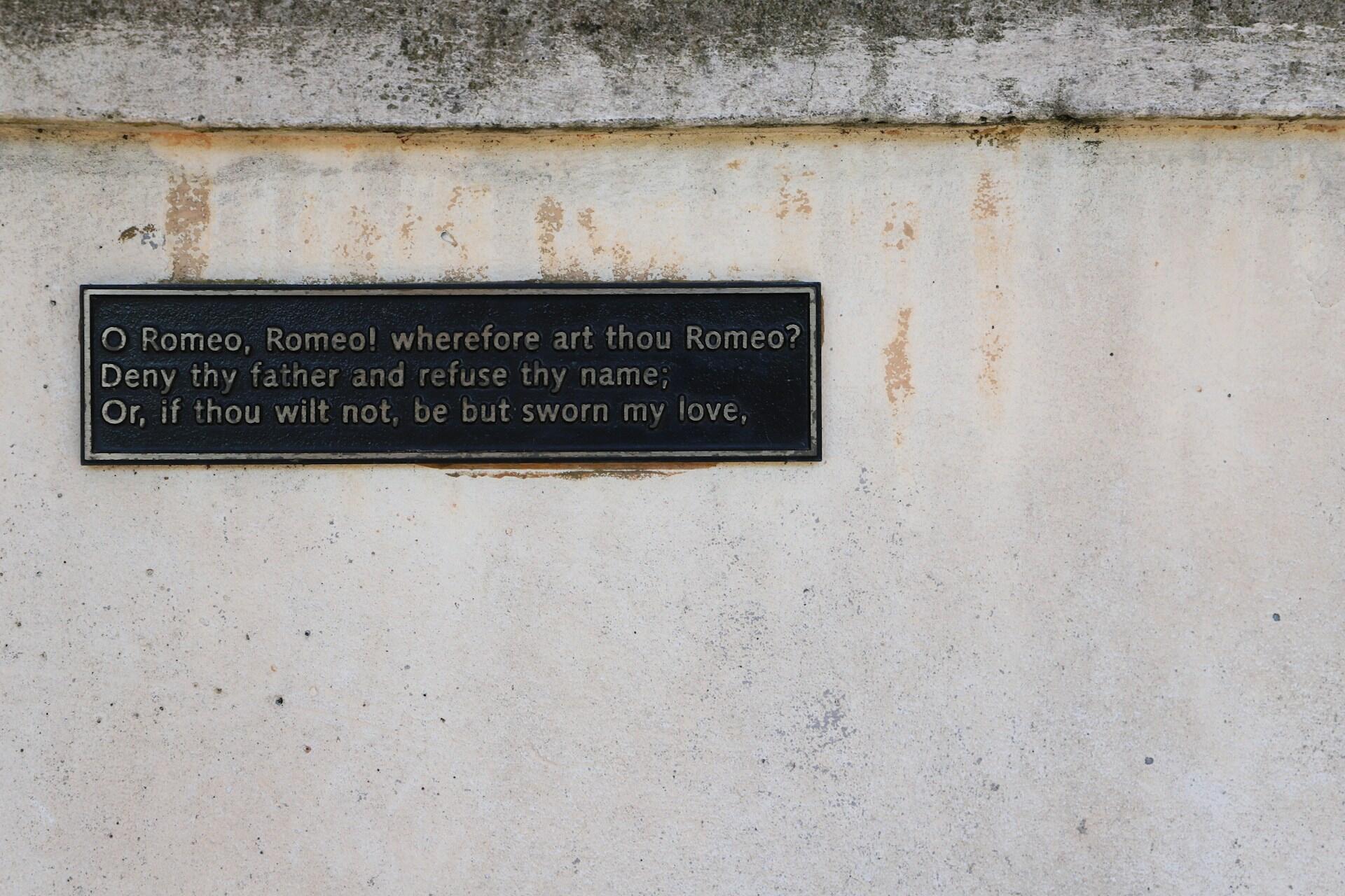 A black plaque on a weathered wall displays a quote from Romeo and Juliet: “O Romeo, Romeo! wherefore art thou Romeo?”