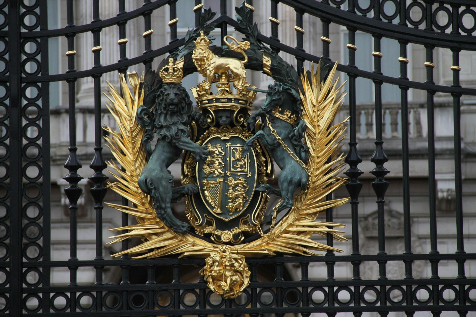 A black wrought-iron gate decorated with a coat of arms featuring a lion and unicorn, with a gold wreath.