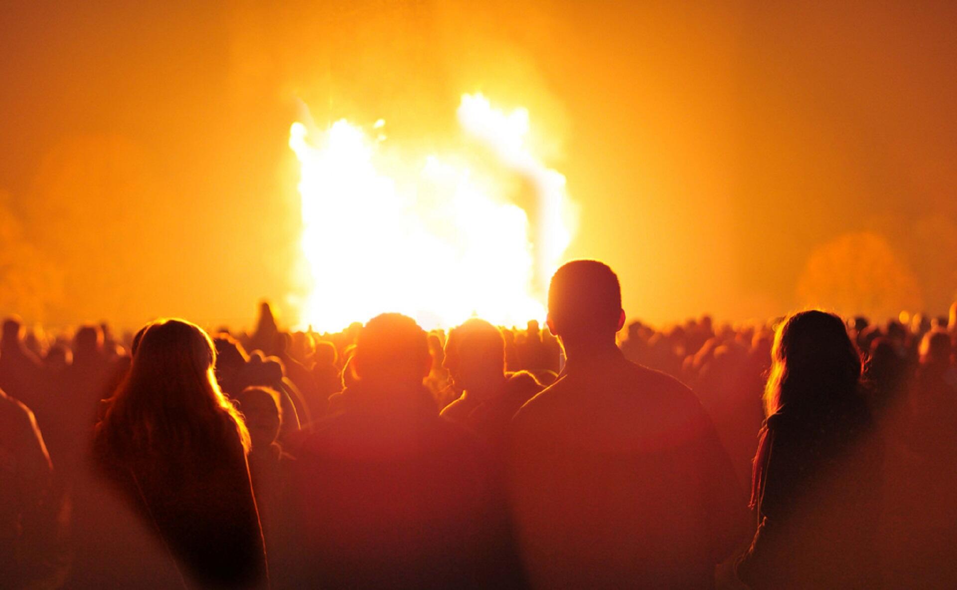 A crowd of people surrounding a large bonfire, giving off a mood of celebration.