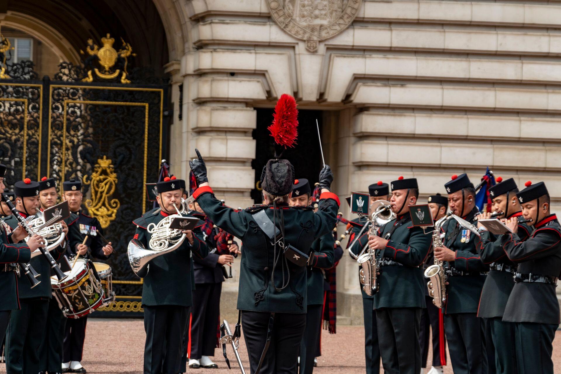 a group of marching band players standing in place and being conducted by a drum major, who is at the front of the formation and holding a small baton