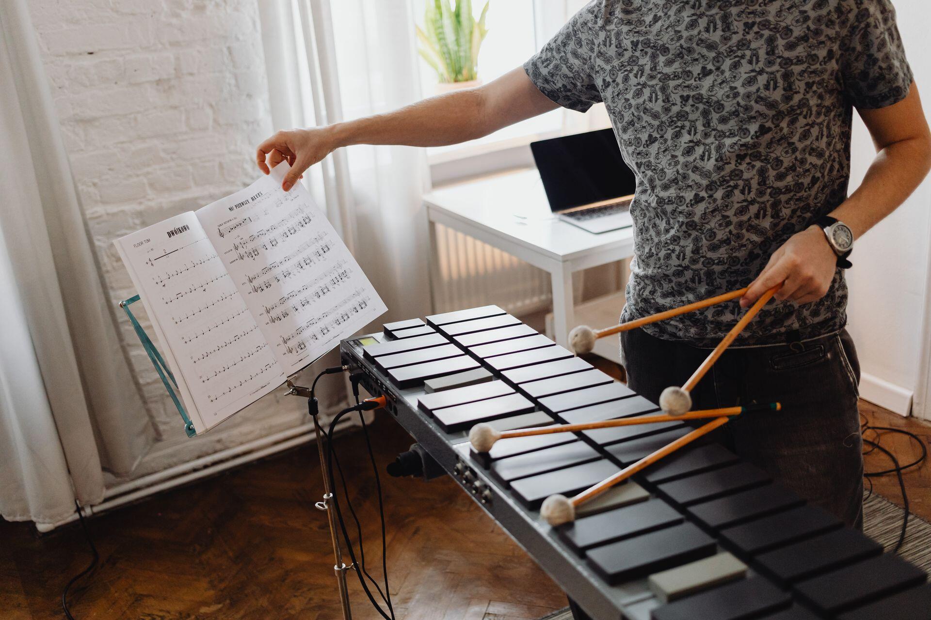 a musician reading sheet music for an electric marimba and holding two mallets in each hand