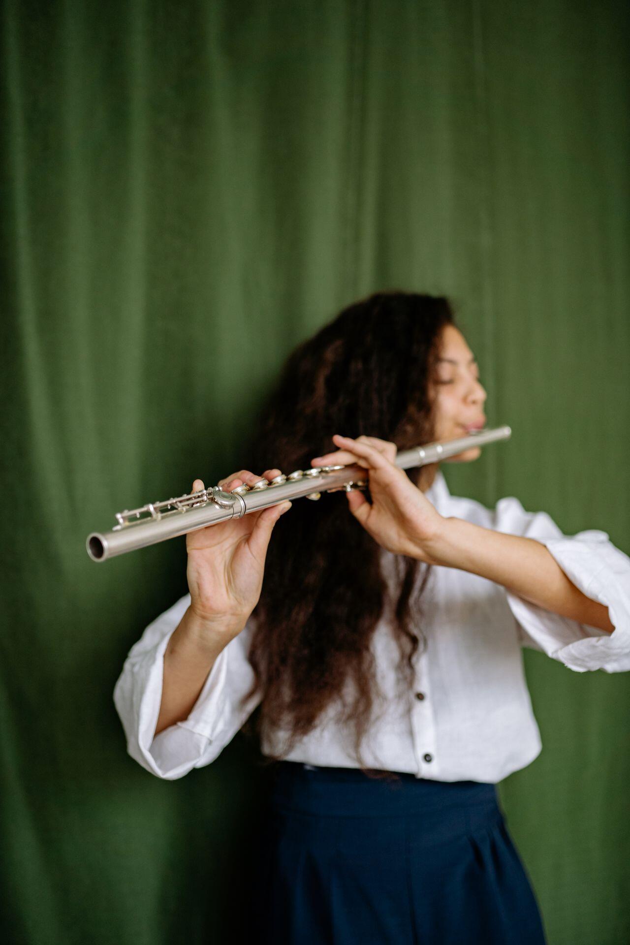 a flute player plays a flute in. front of a rich green curtain background