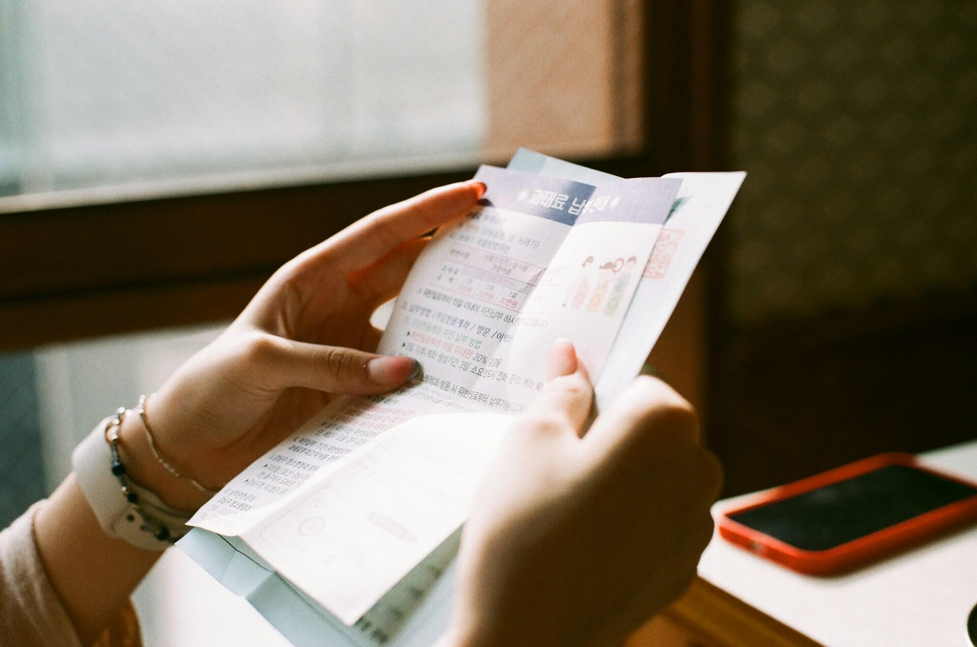 A person with bracelets on their wrist holds sheets of paper in both hands, examining them.