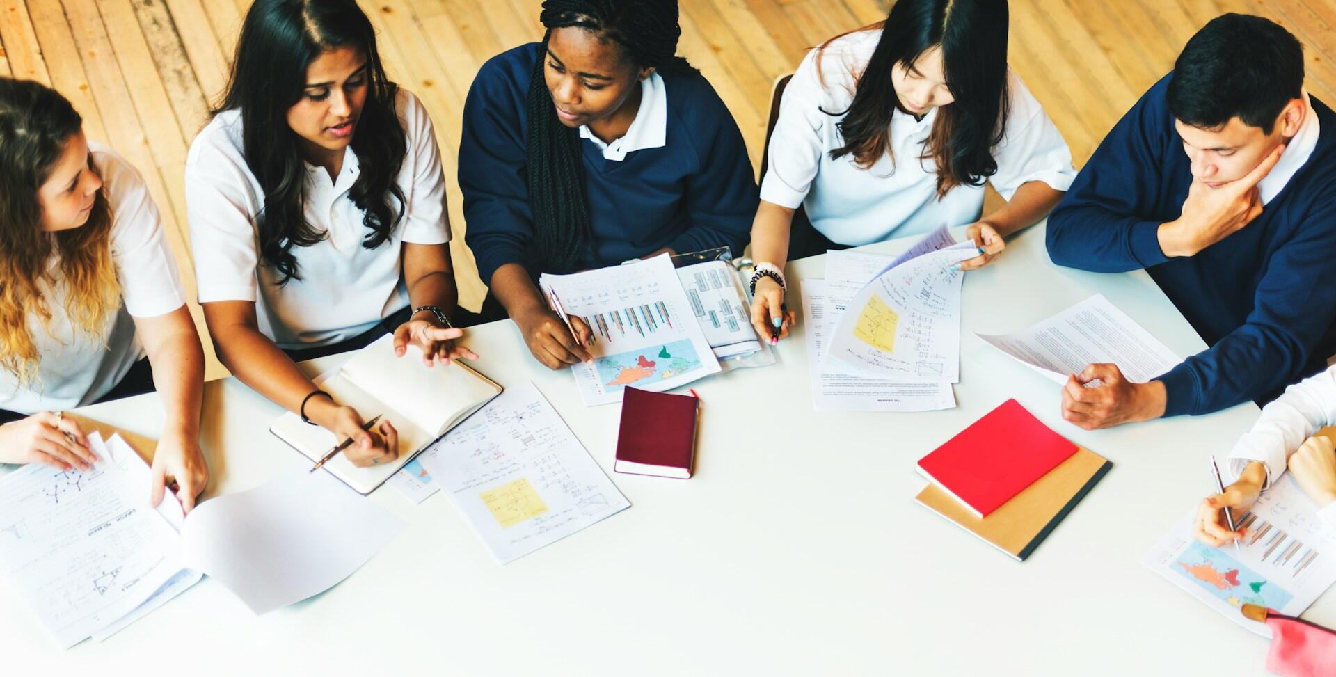 A group of students collaborates at a table, surrounded by papers and books, engaged in a study session.