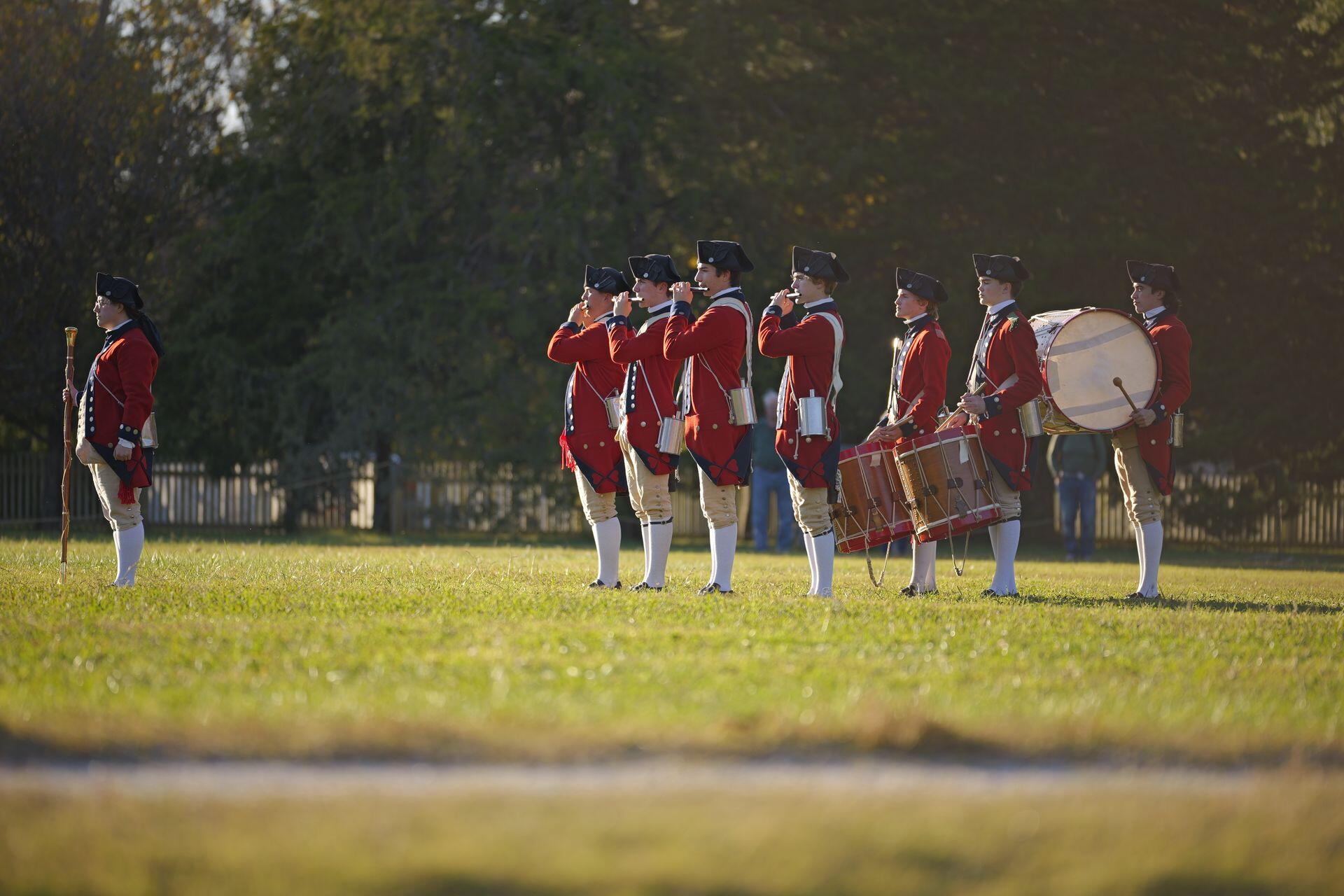 a line of historical reenactors with red coats, fifes and drums, with a drum major at the front