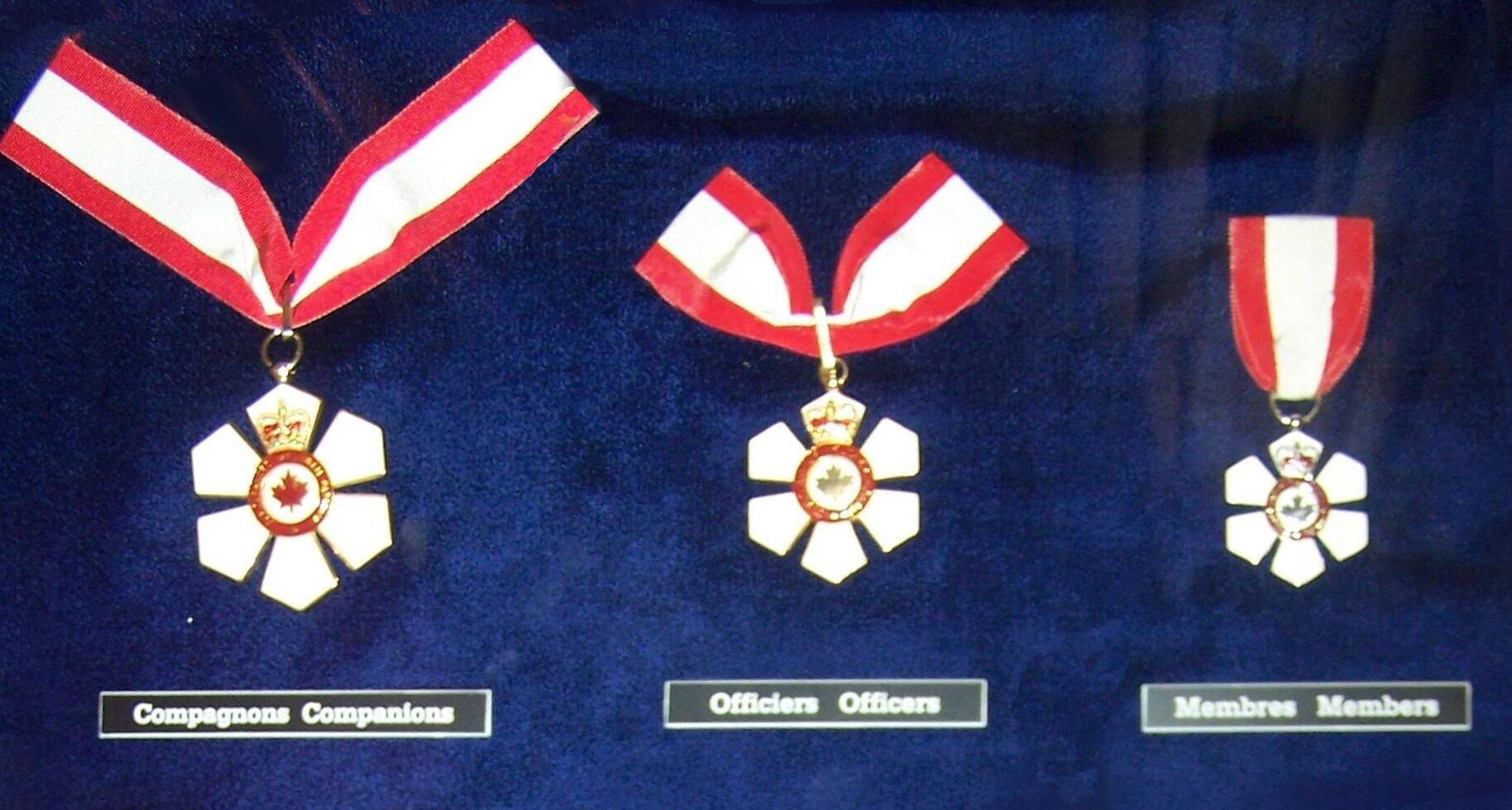 Three white-and-red maple leaf medals on blue fabric are labeled “Compagnons Companions,” “Officiers Officers,” and “Membres Members.”