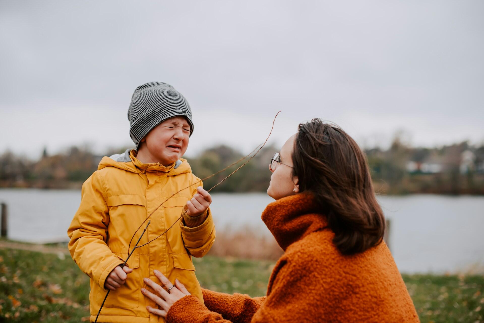 A woman with brown hair squats down to face a crying child. The mood is stressed, echoed in the cloudy, cold day.