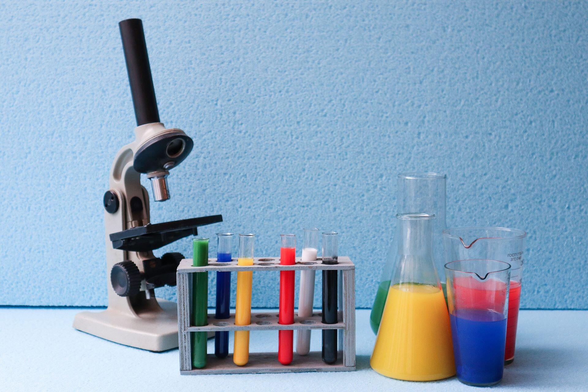 Microscope, test tubes and laboratory glassware containing colourful chemical solutions.