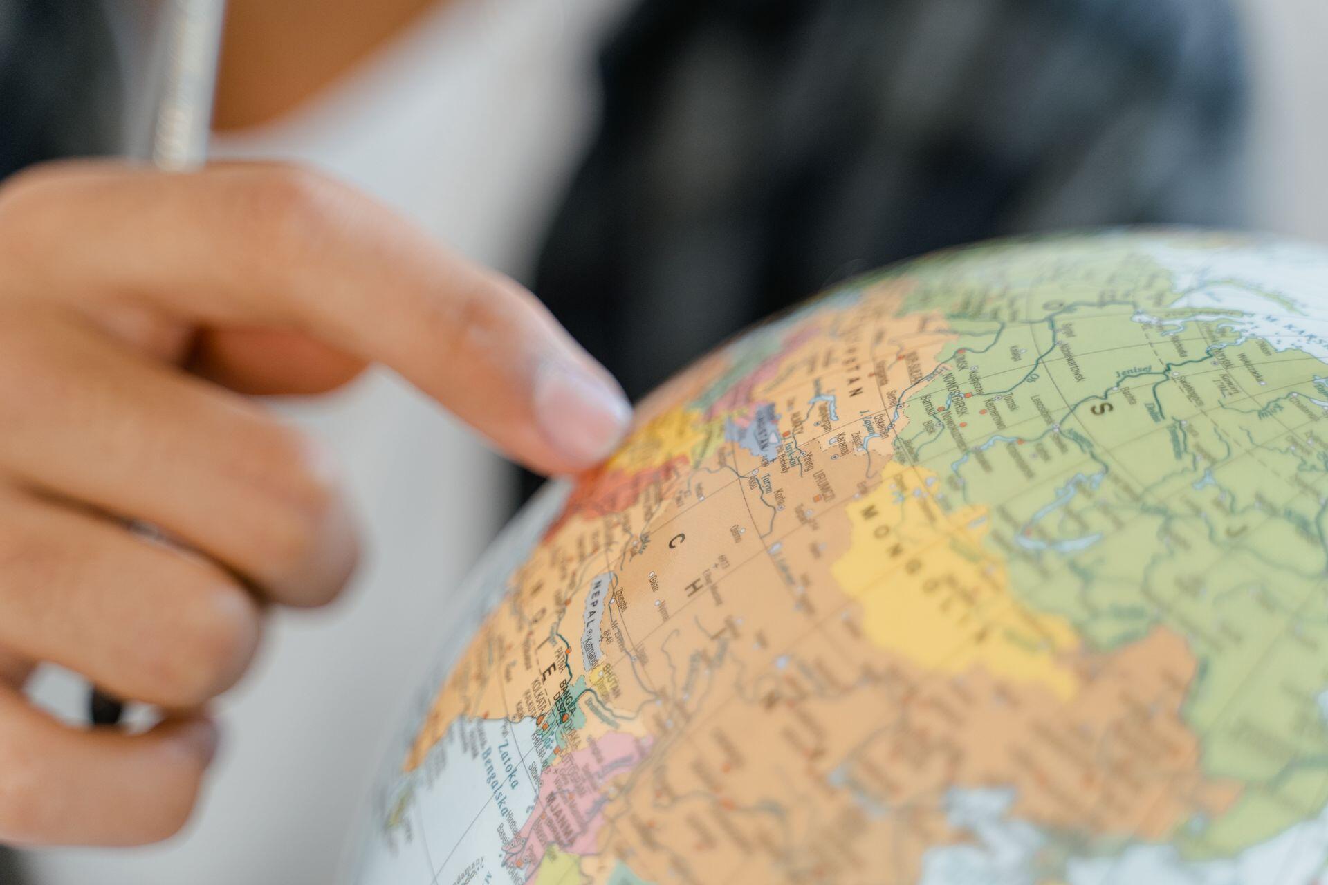 A person points to a location on a colorful globe, with parts of Europe, Africa, and Asia visible.