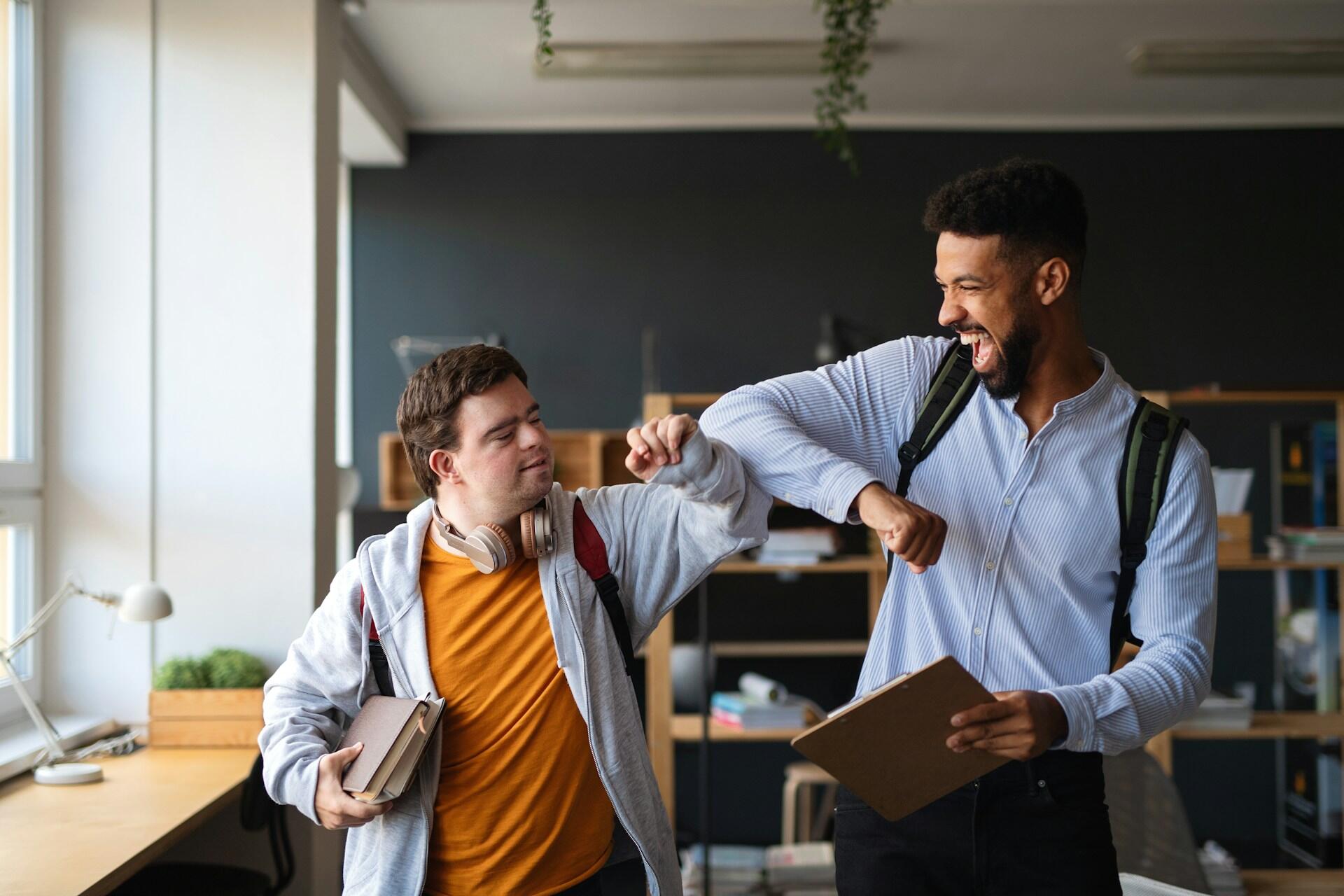 An older person bumps elbows with a special needs student in a classroom, giving of a friendly, vibrant mood.