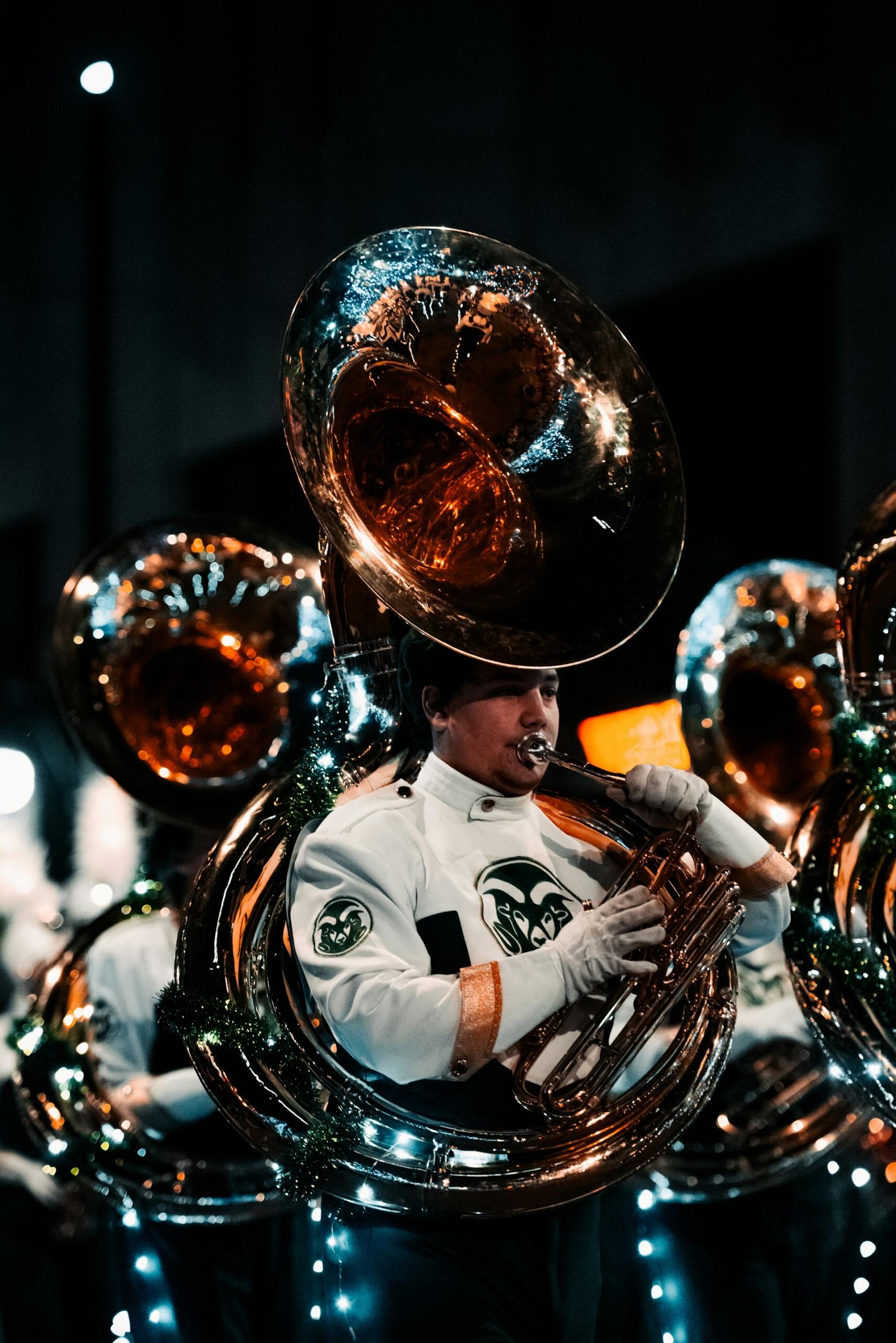 sousaphone players in a marching band playing their instruments while wearing marching regalia