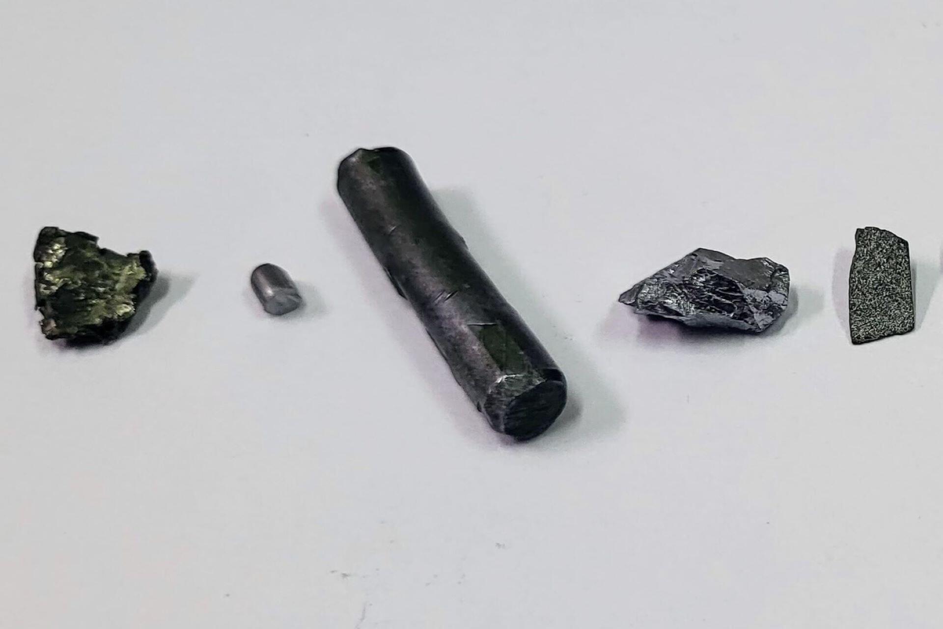 Several dark metallic transition metal samples arranged on a white surface.