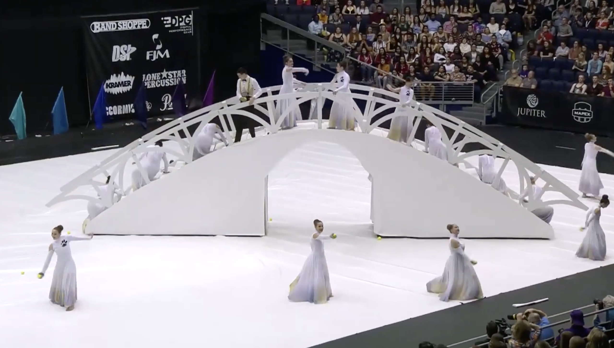 a still from a video of a color guard in the winter guard competition featuring a large bridge with several people dancing on it