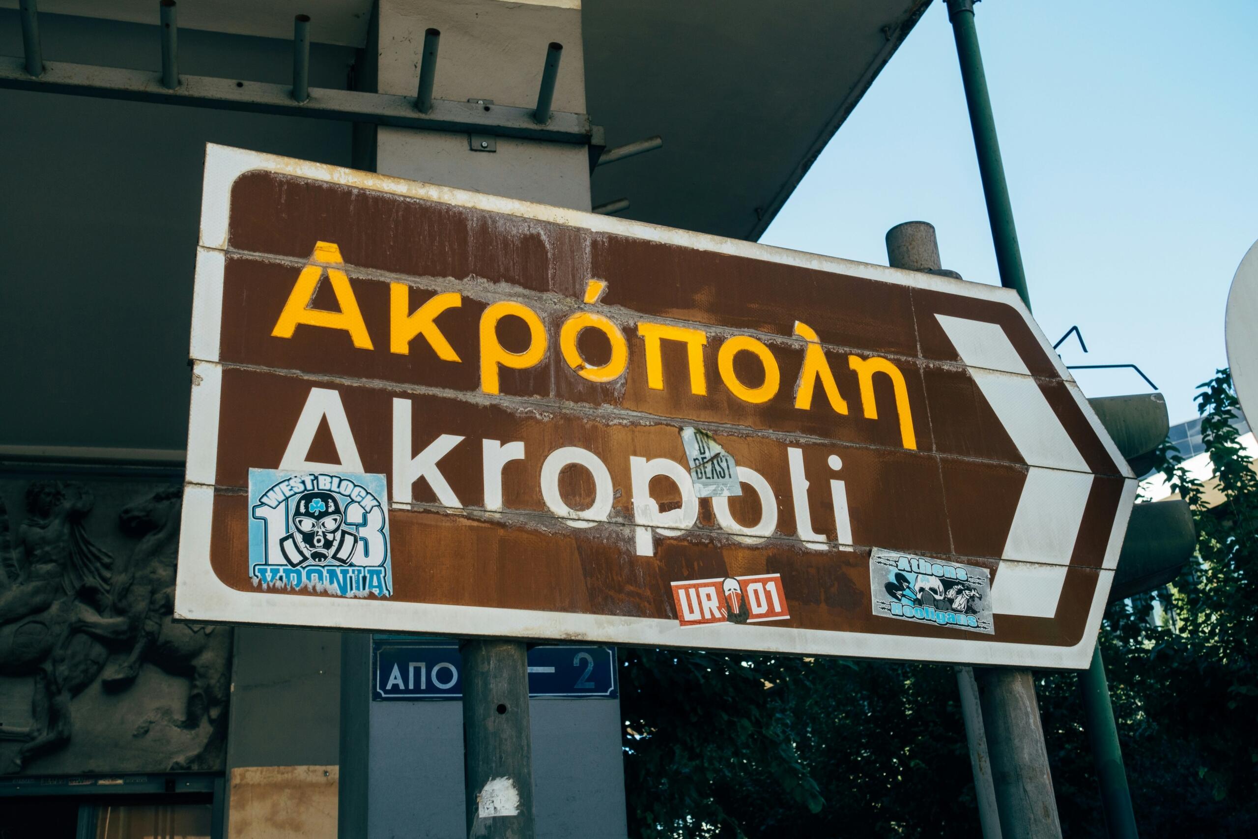 Πινακίδα κατεύθυνσης προς την Ακρόπολη με τη λέξη «Ακρόπολη» γραμμένη στα ελληνικά και στα λατινικά.