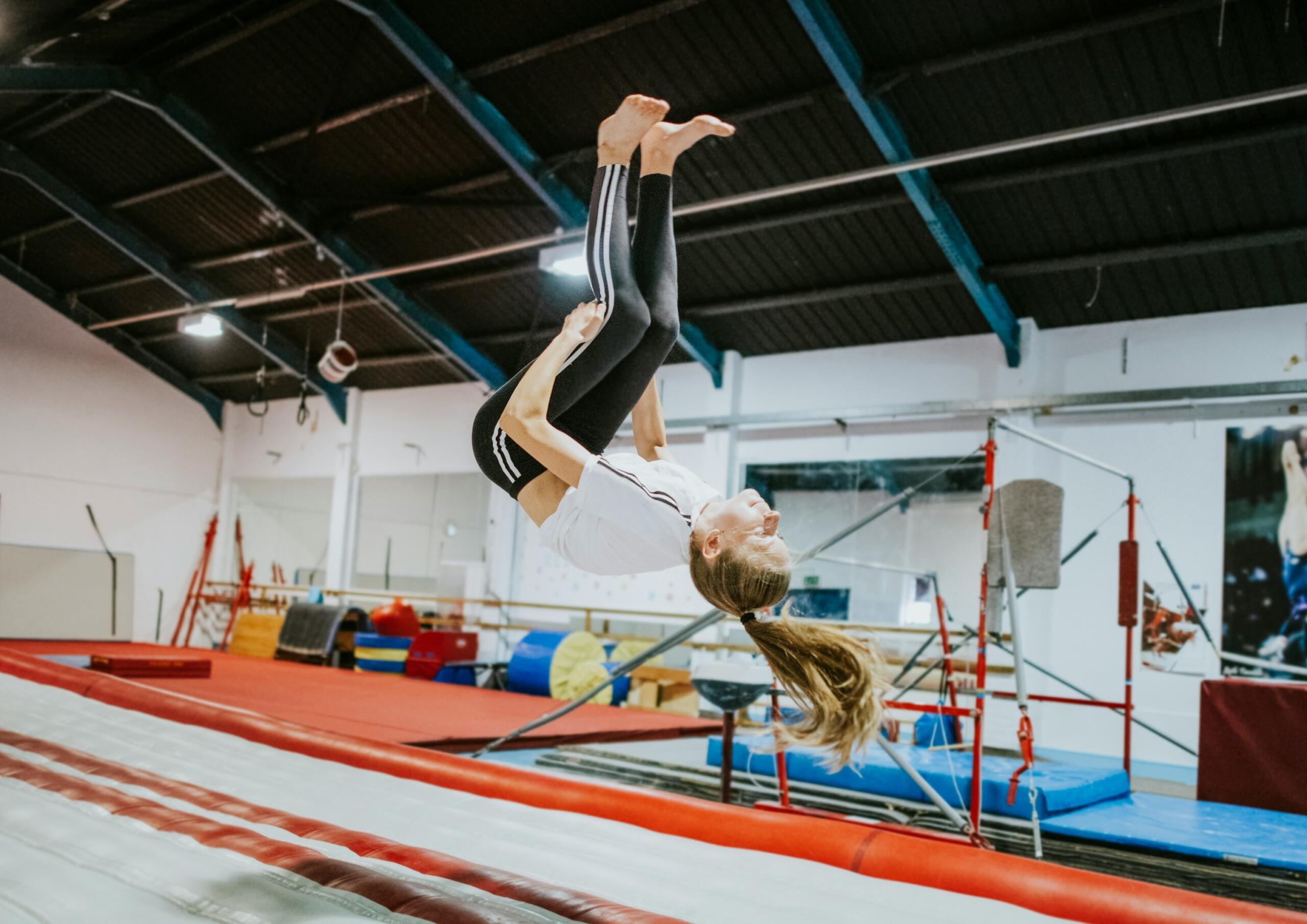 Αθλήτρια εκτελεί ακροβατικό άλμα σε χώρο ενόργανης γυμναστικής.