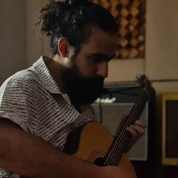 Άνδρας παίζει ακουστική κιθάρα σε εσωτερικό χώρο, εξασκώντας μουσικό κομμάτι.