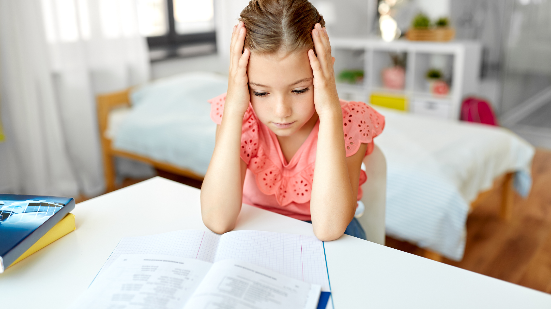 Μαθήτρια διαβάζει στο γραφείο της στο σπίτι και δείχνει συγκεντρωμένη πάνω στο ανοιχτό τετράδιο.