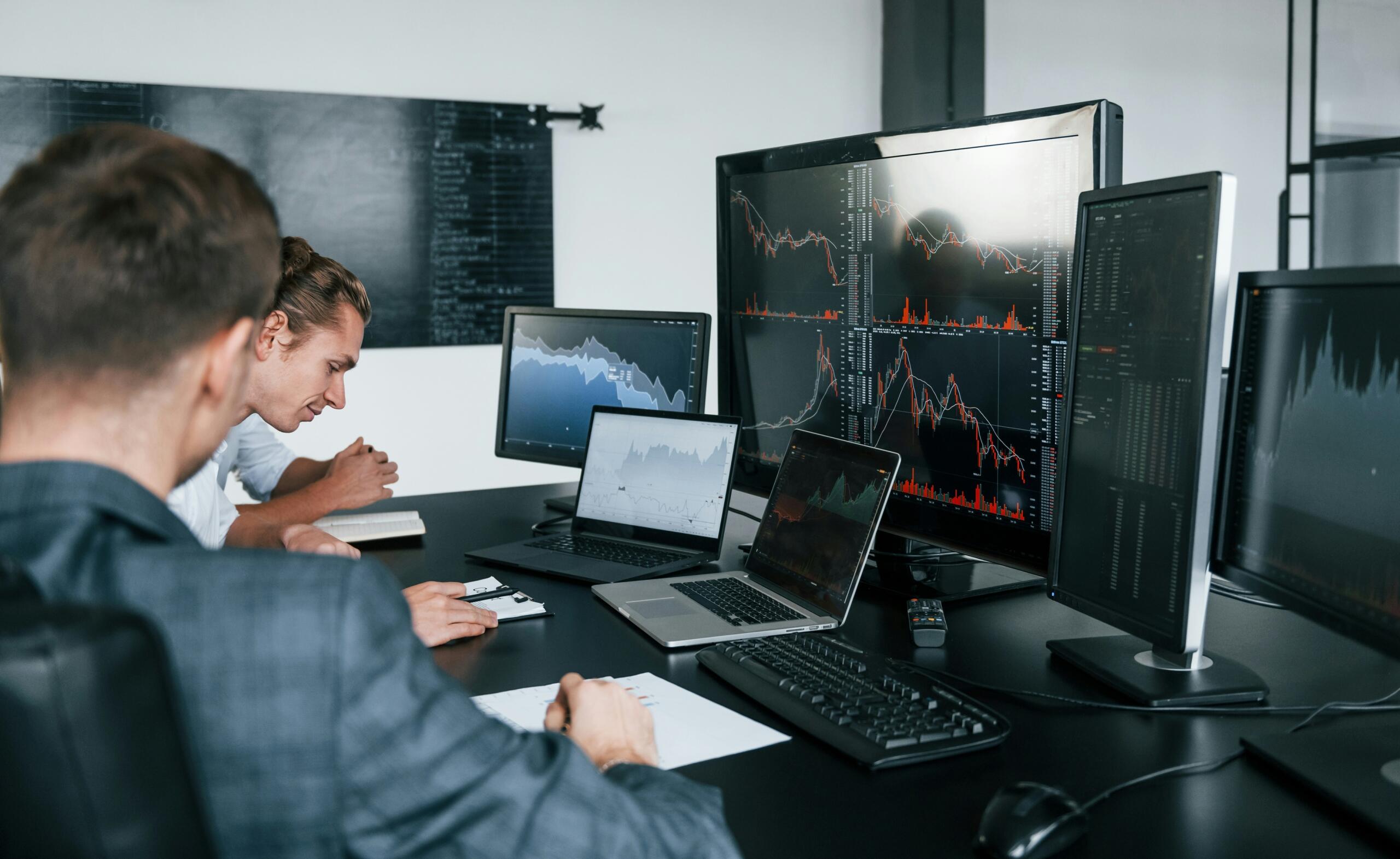 Επαγγελματίες αναλύουν χρηματοοικονομικά δεδομένα σε πολλαπλές οθόνες υπολογιστών σε γραφείο.