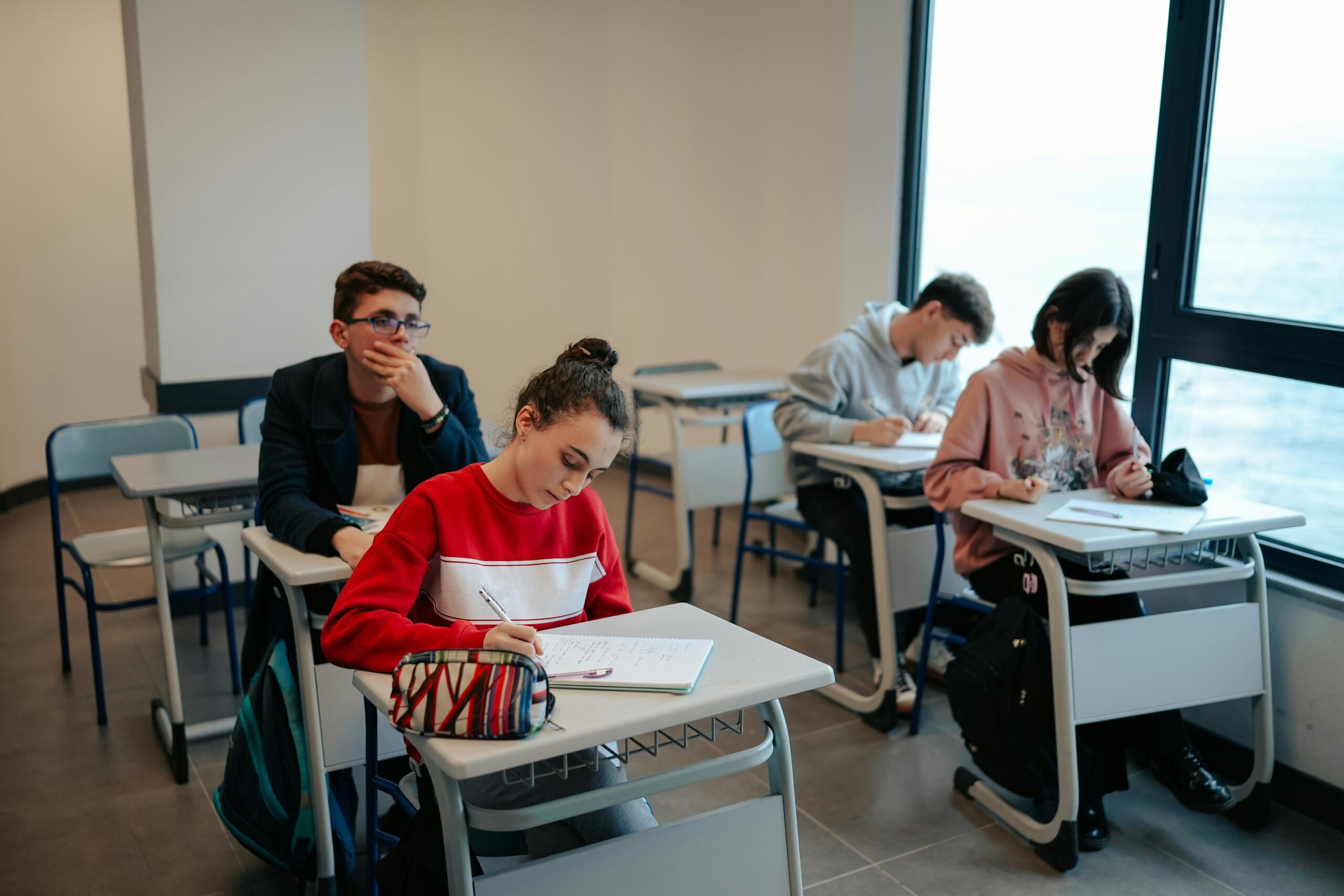 Μαθητές λυκείου γράφουν και παρακολουθούν μάθημα σε σύγχρονη σχολική αίθουσα.