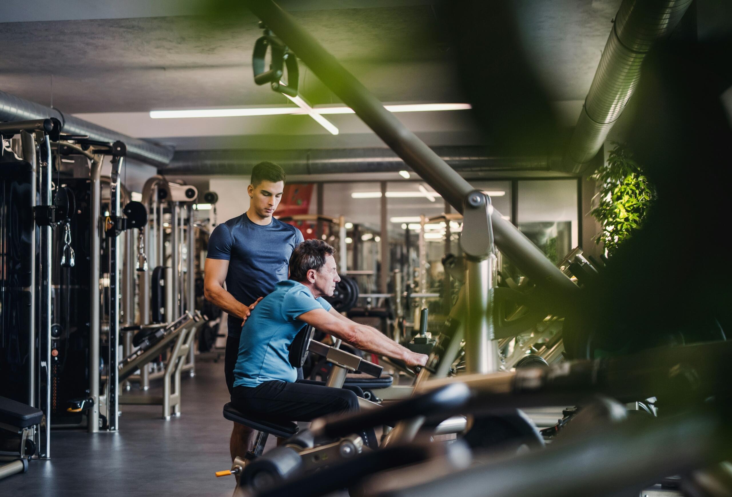 Personal trainer βοηθά άνδρα σε άσκηση με μηχάνημα στο γυμναστήριο.