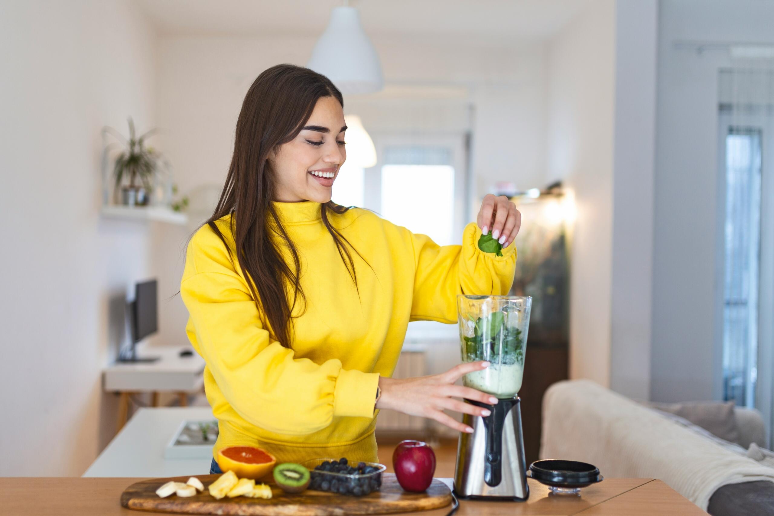 Γυναίκα ετοιμάζει πράσινο smoothie σε μπλέντερ με φρούτα και λαχανικά.