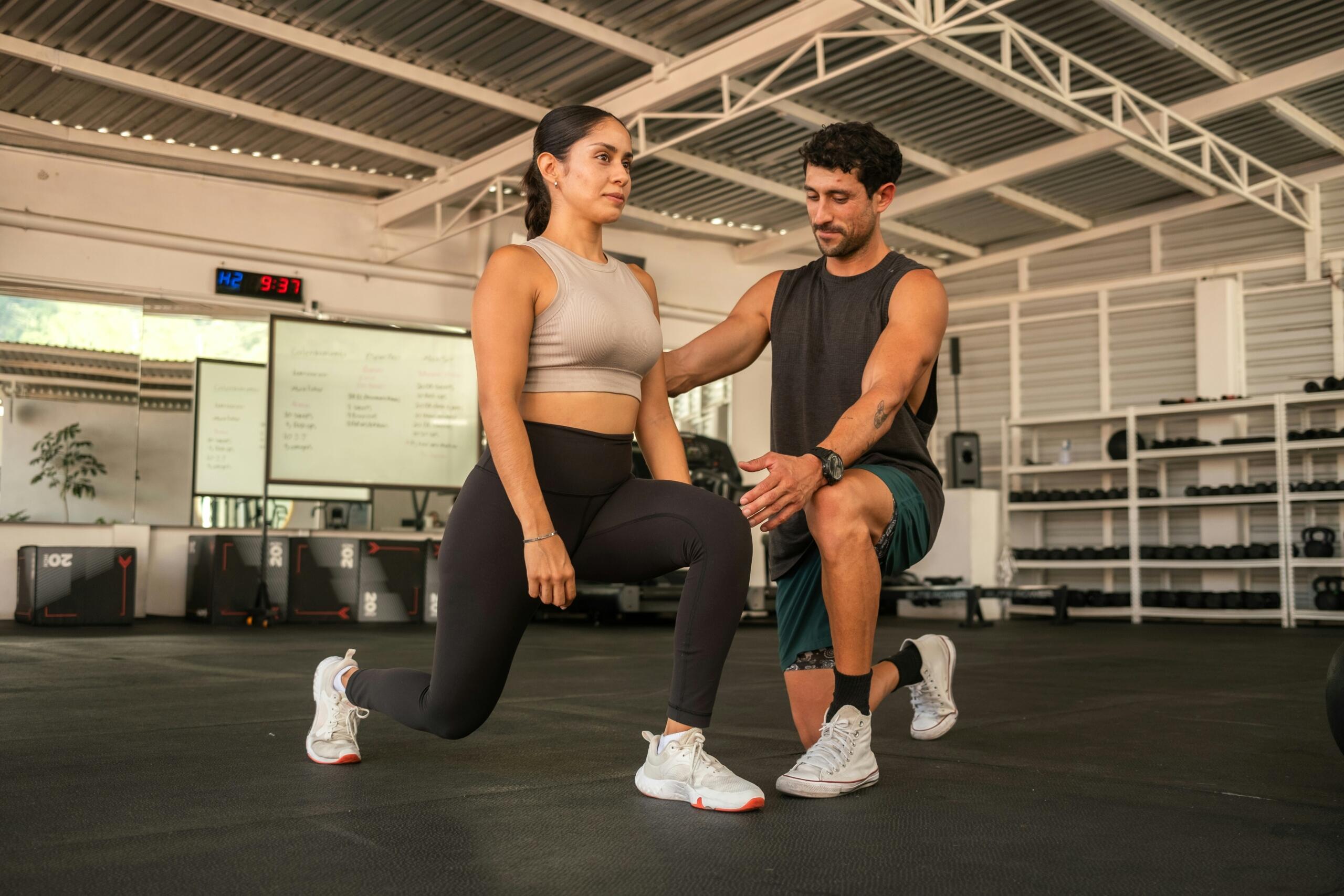 Personal trainer καθοδηγεί γυναίκα σε άσκηση προβολών στο γυμναστήριο.