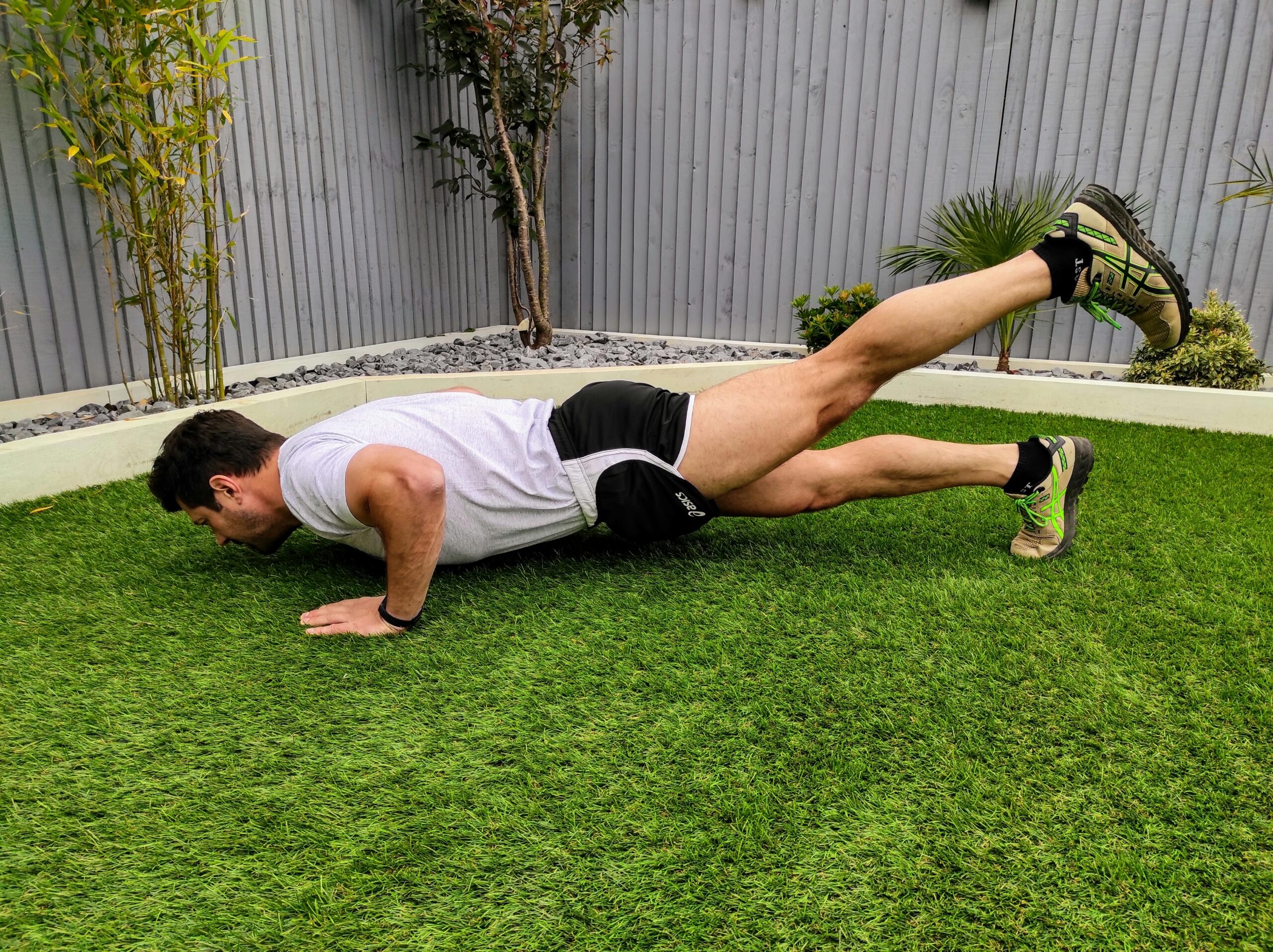 Άνδρας κάνει push-ups με ανύψωση ποδιού σε κήπο εξωτερικού χώρου.