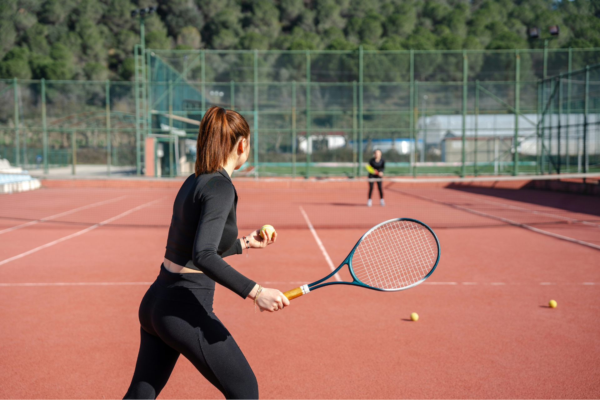 Αθλήτρια ετοιμάζεται να σερβίρει σε γήπεδο τένις, κρατώντας ρακέτα και μπαλάκι κατά τη διάρκεια προπόνησης.