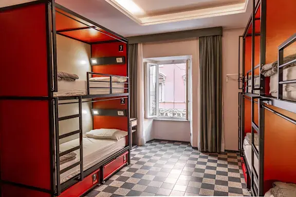 Σύγχρονος κοιτώνας hostel στη Ρώμη με κουκέτες, φωτεινό εσωτερικό και μεγάλο παράθυρο.