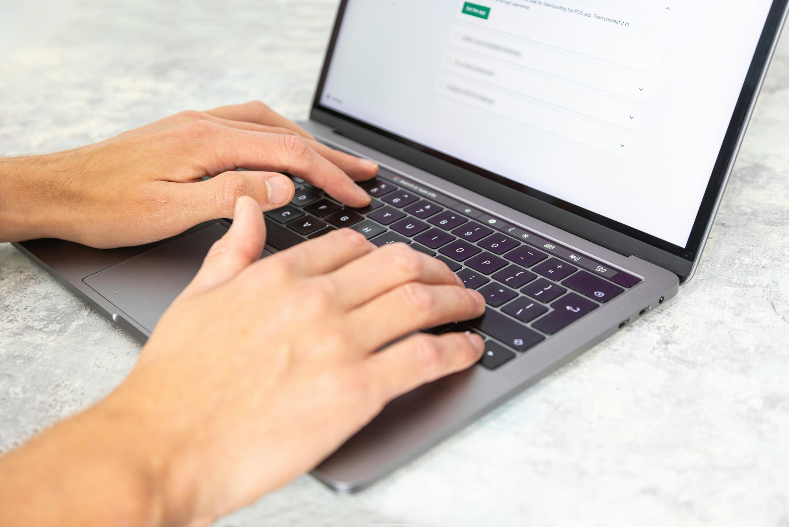 Κοντινό πλάνο χεριών πληκτρολογούν σε laptop με ιστοσελίδα ανοιχτή στην οθόνη