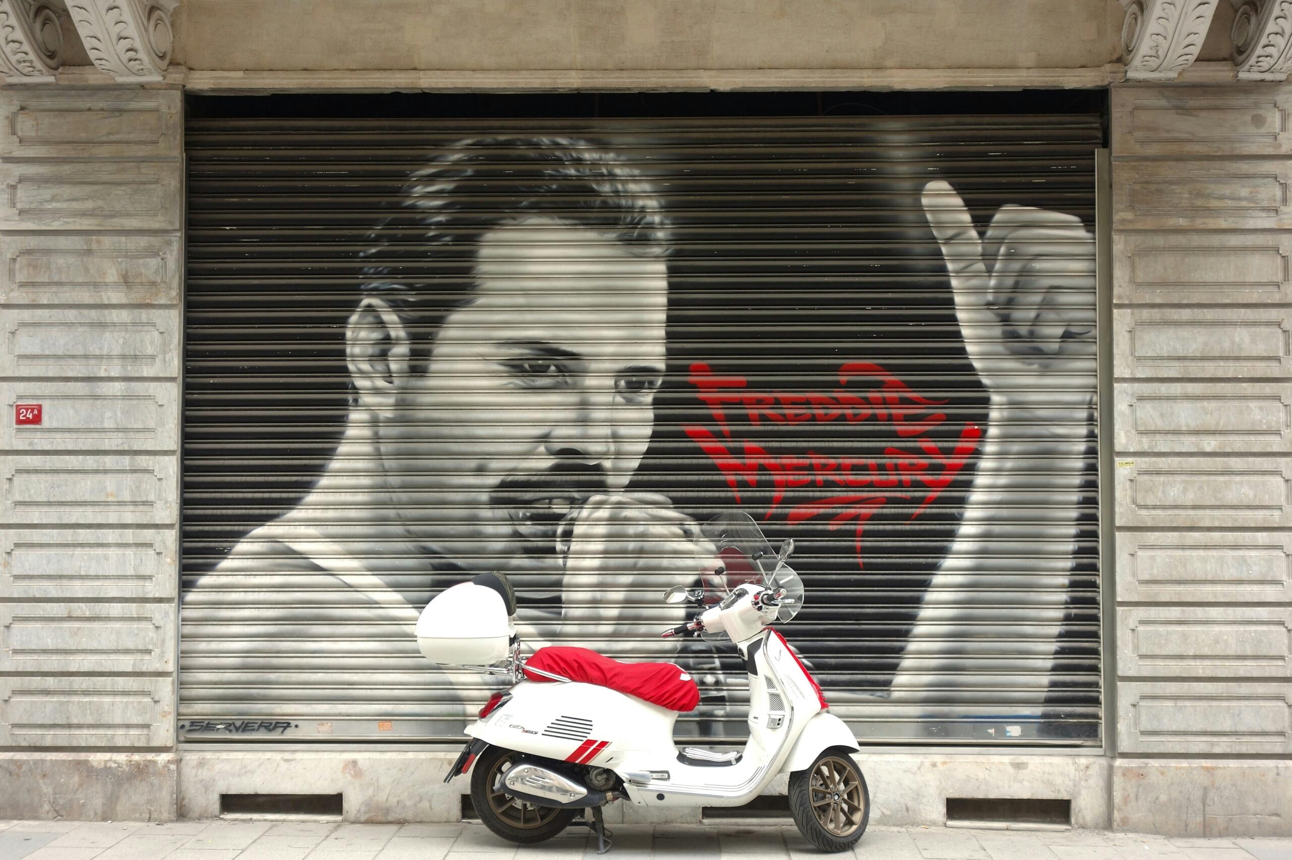 Τοιχογραφία του Freddie Mercury σε ρολό ασφαλείας καταστήματος, με λευκή μηχανή σκούτερ σταθμευμένη μπροστά