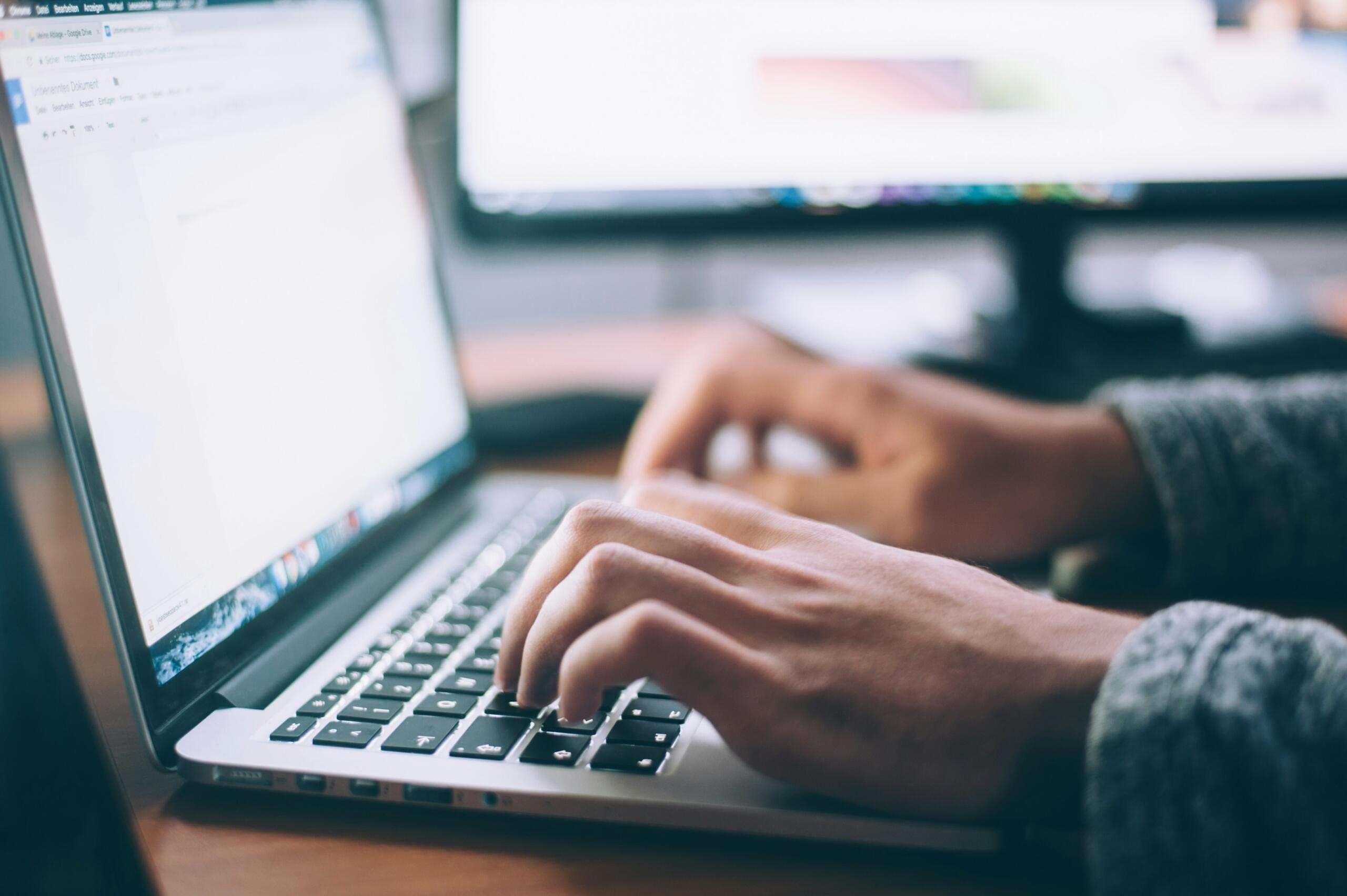 Χέρια πληκτρολογούν σε laptop με ανοιχτό έγγραφο Google Docs στην οθόνη