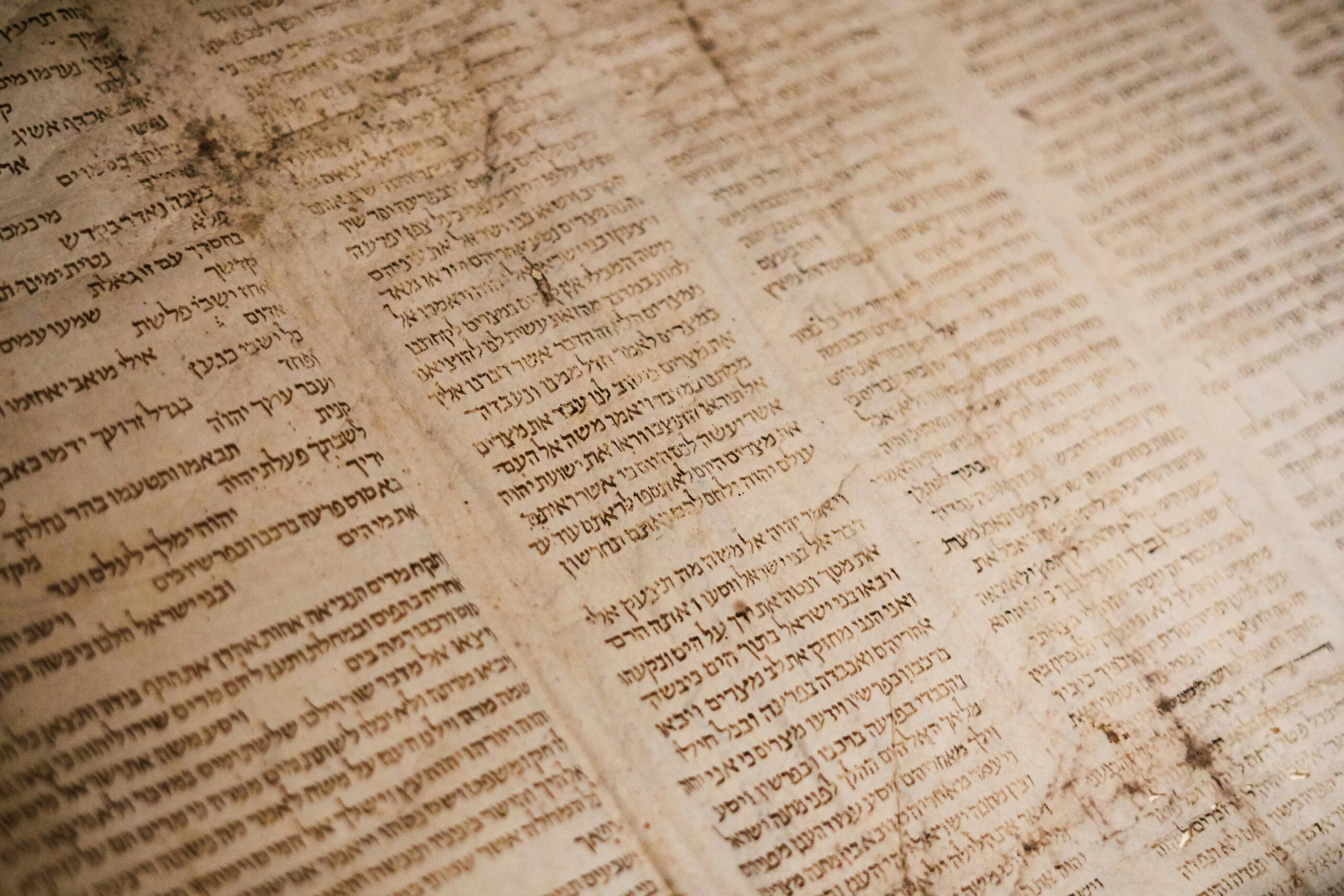 Παλιό χειρόγραφο περγαμηνής με εβραϊκό κείμενο σε στήλες, φθαρμένο από τον χρόνο με κιτρινισμένο χαρτί και σκουρόχρωμα σημάδια φθοράς