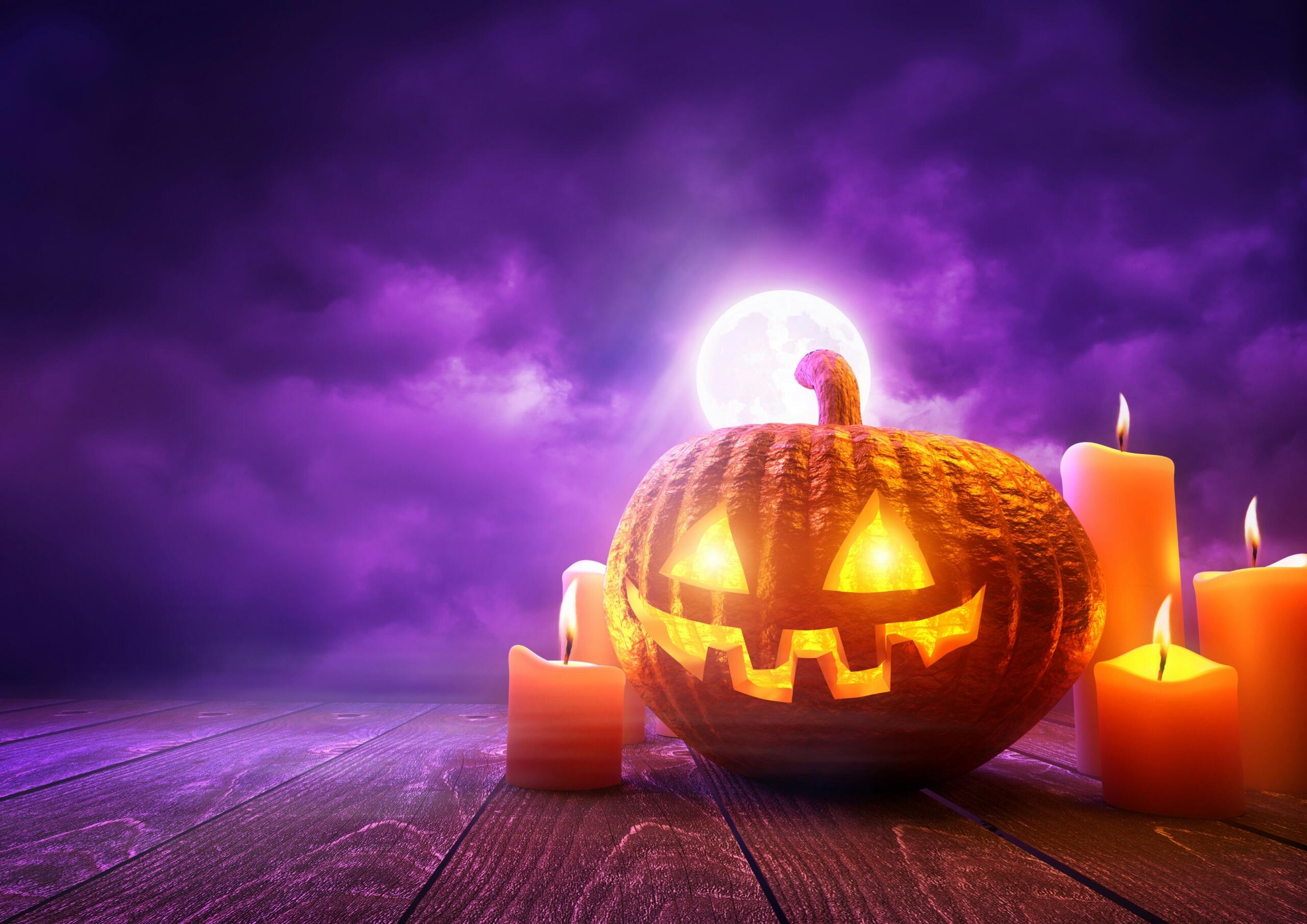 Σκαλισμένη κολοκύθα του Halloween με αναμμένο πρόσωπο, περιτριγυρισμένη από κεριά, μπροστά σε μωβ νυχτερινό ουρανό με πανσέληνο.