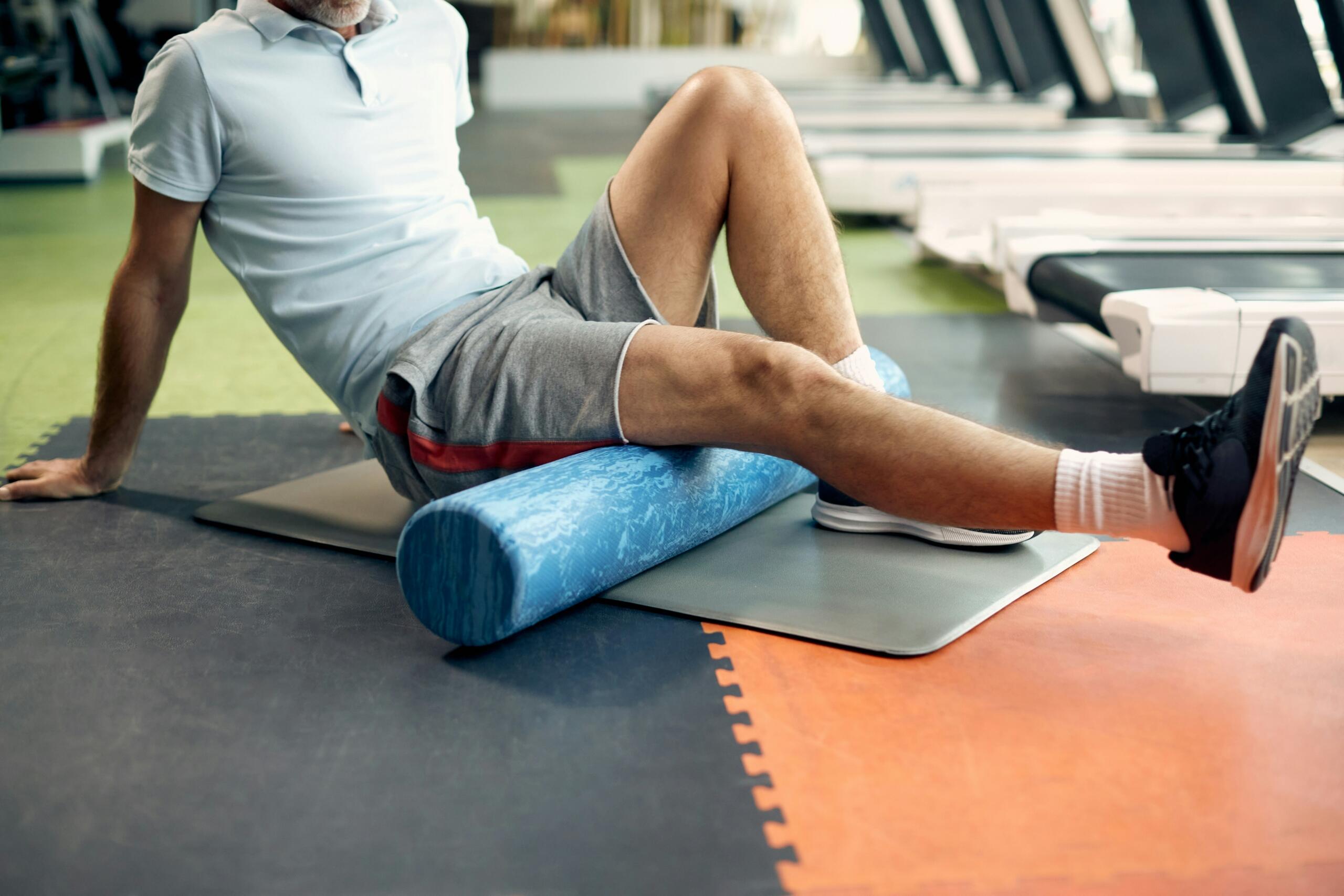 Άντρας κάνει διατάσεις ποδιού με foam roller πάνω σε στρώμα γυμναστικής.