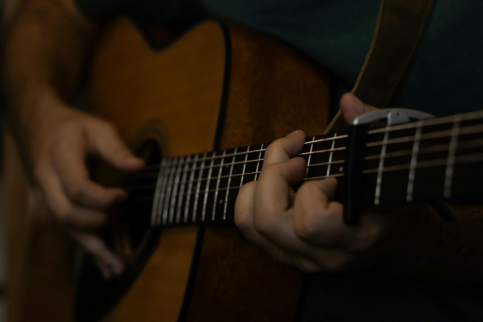 Close-up of a hand forming chords on an acoustic guitar with a capo