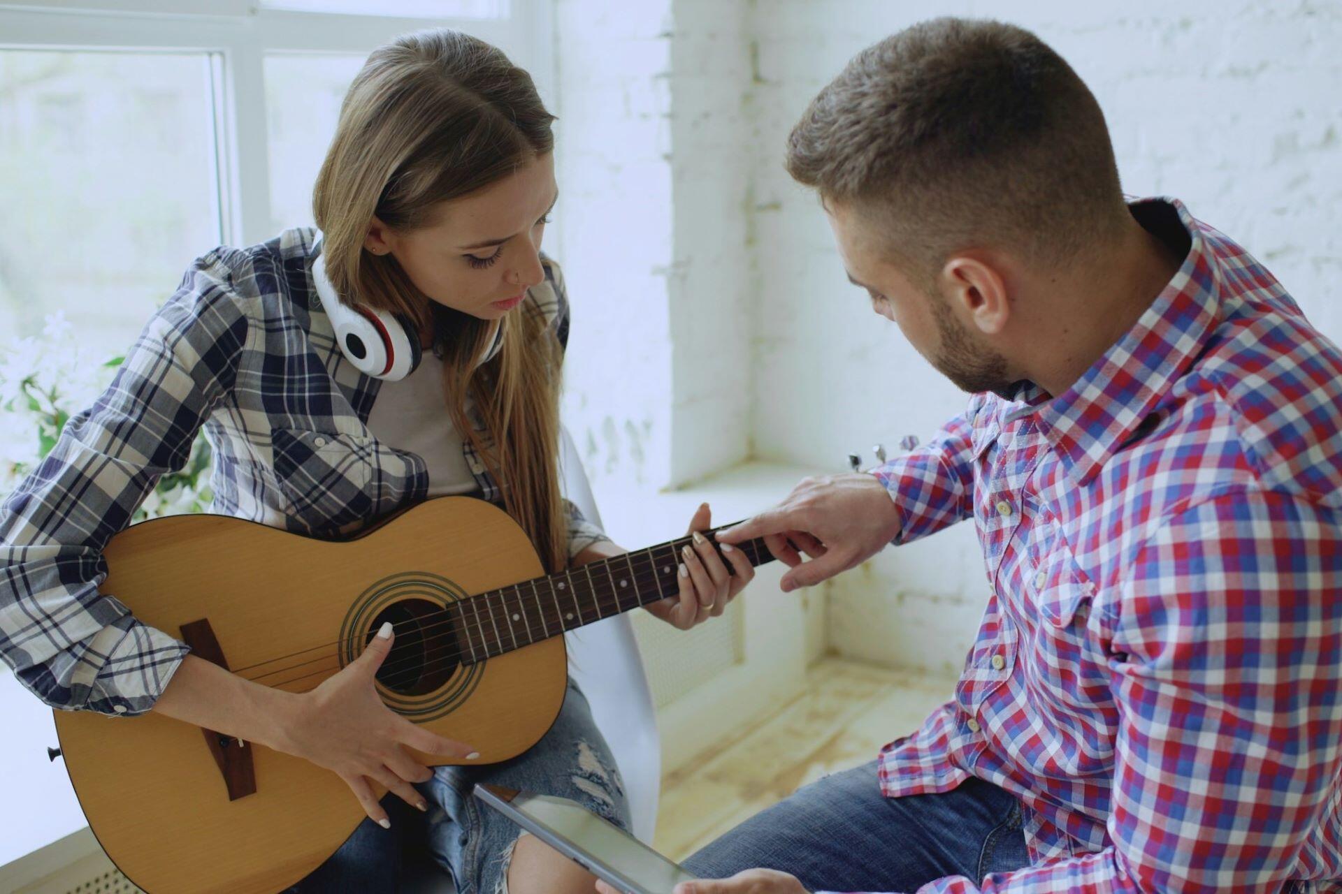 Guitar tutor showing a student where to place her fingers on the fretboard