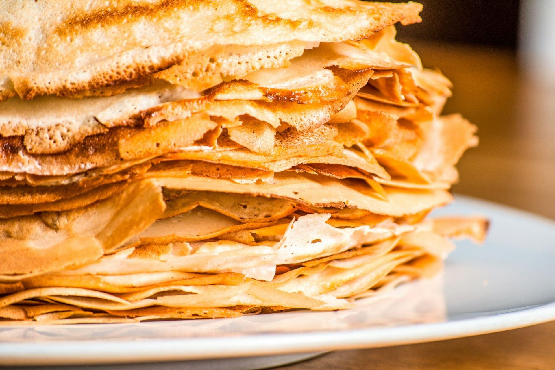 Stack of thin golden crêpes on a white plate