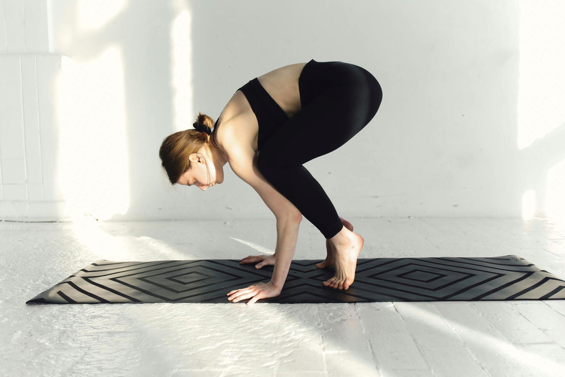 Woman practising a beginner crow pose with hands on the mat and toes still touching the floor